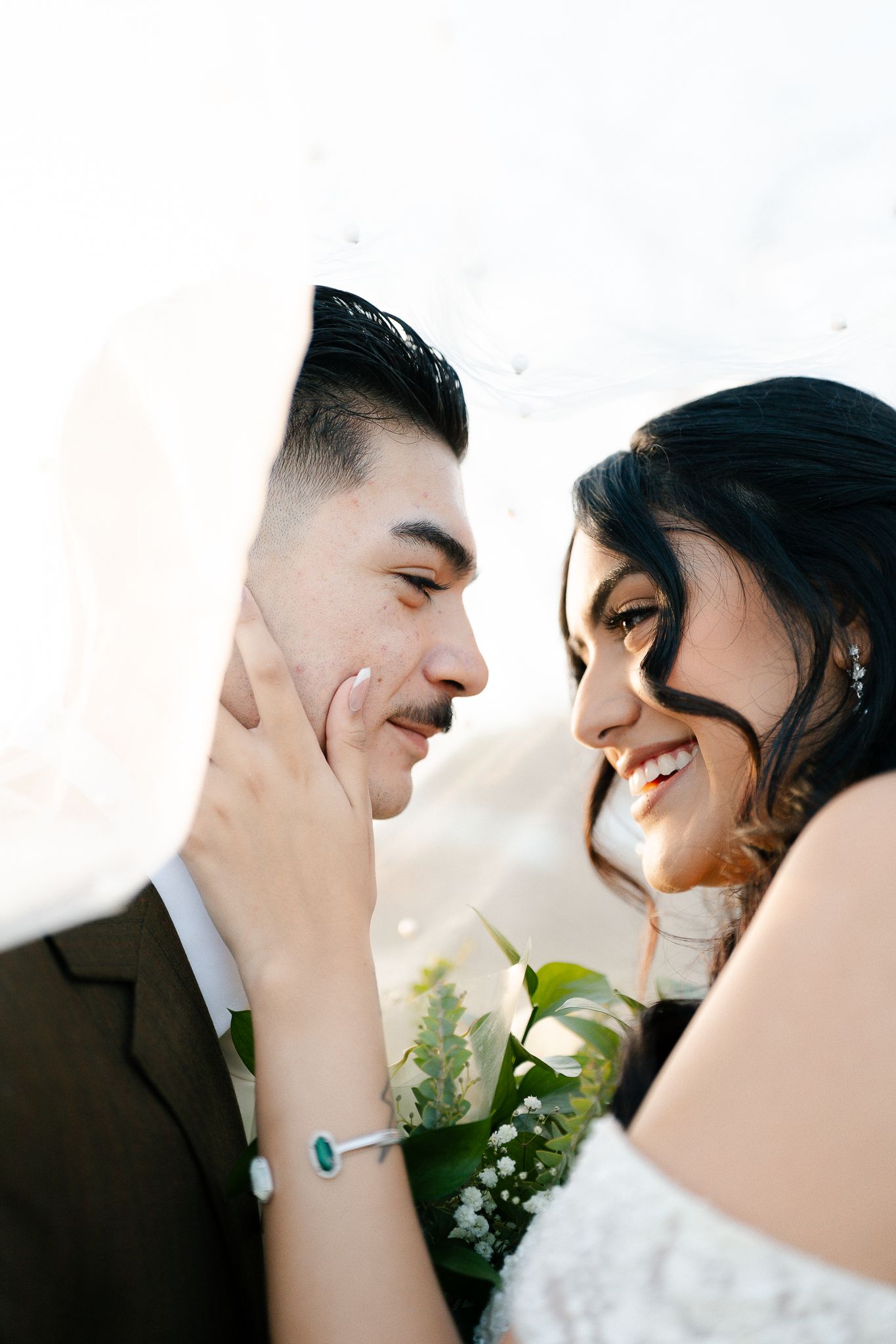 A romantic wedding portrait shows a tender moment between newlyweds against a bright background.