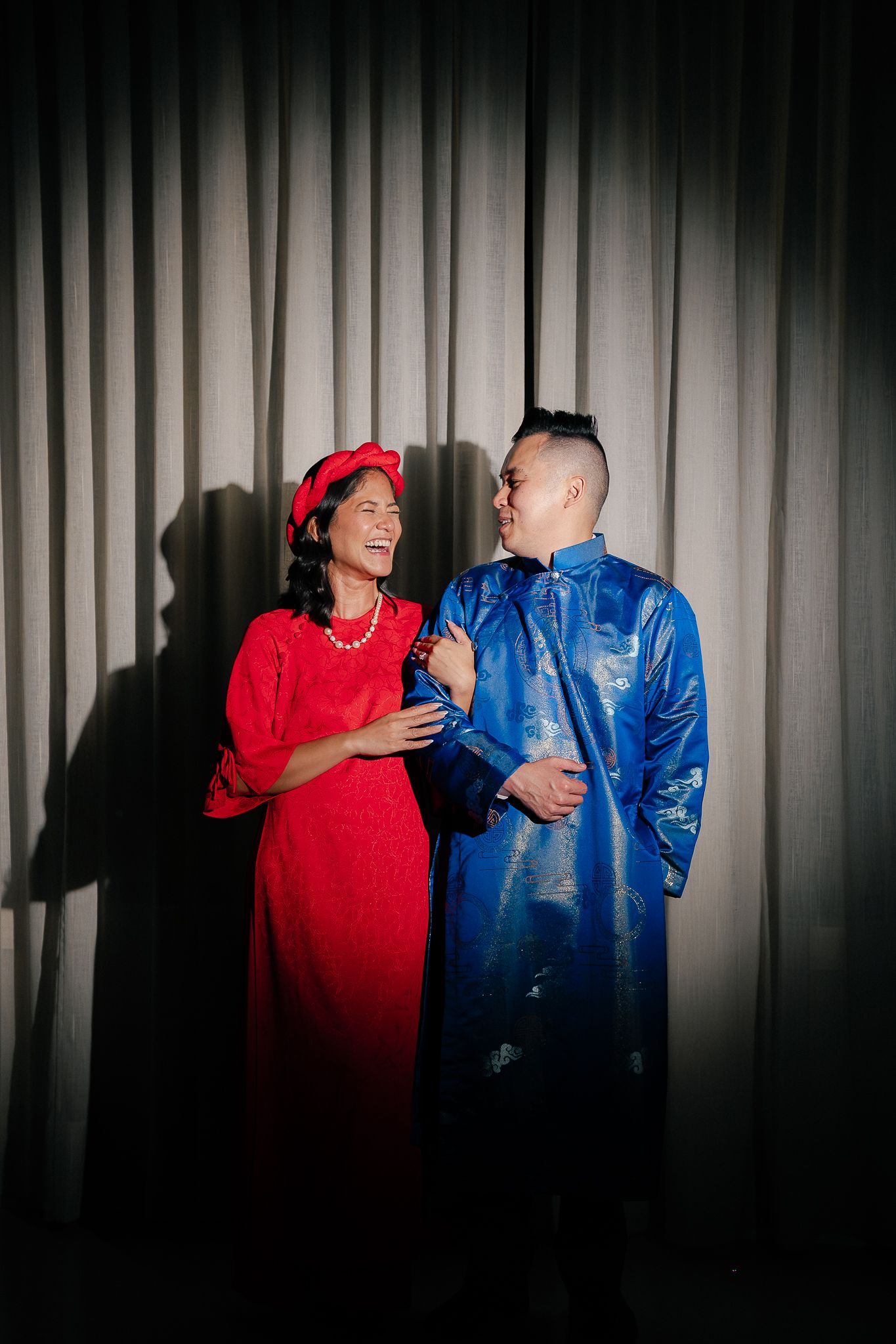A couple in red and blue outfits dancing together in front of a white curtain background.