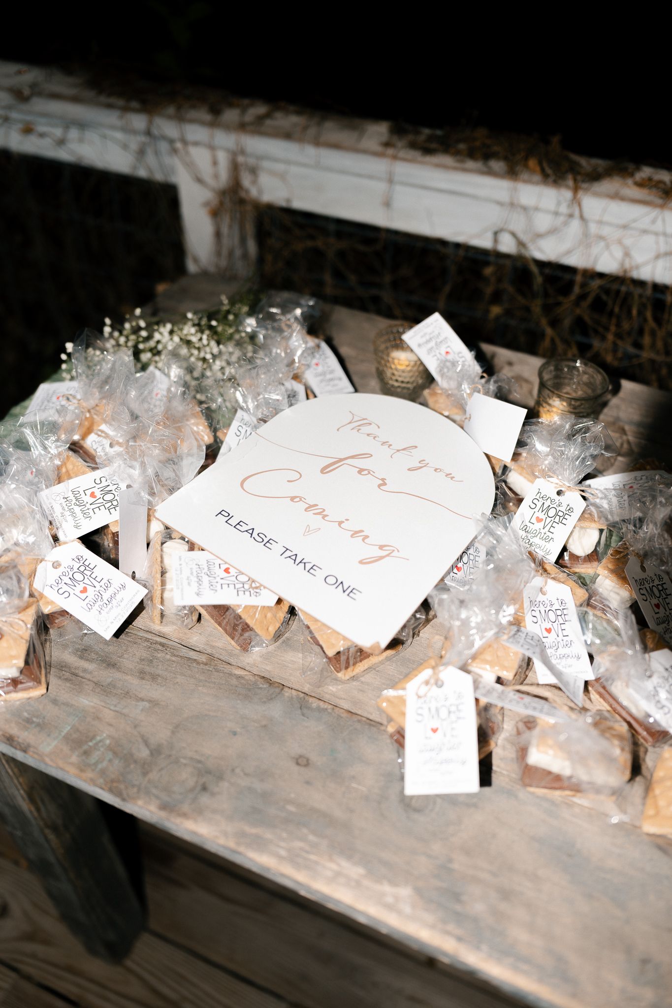 Wedding favor bags with handwritten notes arranged in a row on a vintage wooden surface.