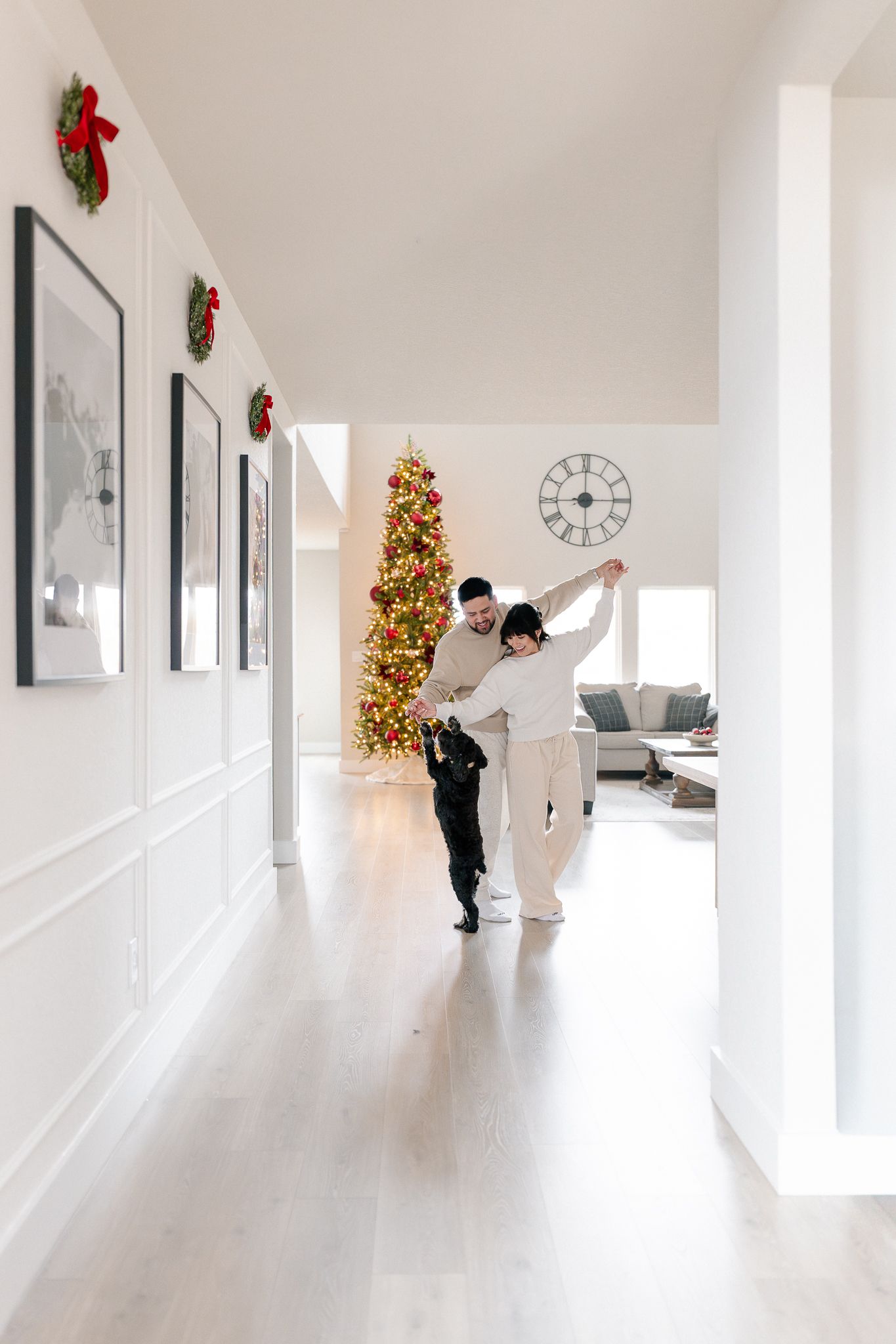 Two people dancing in a bright white hallway decorated for Christmas with a lit tree visible in the background.