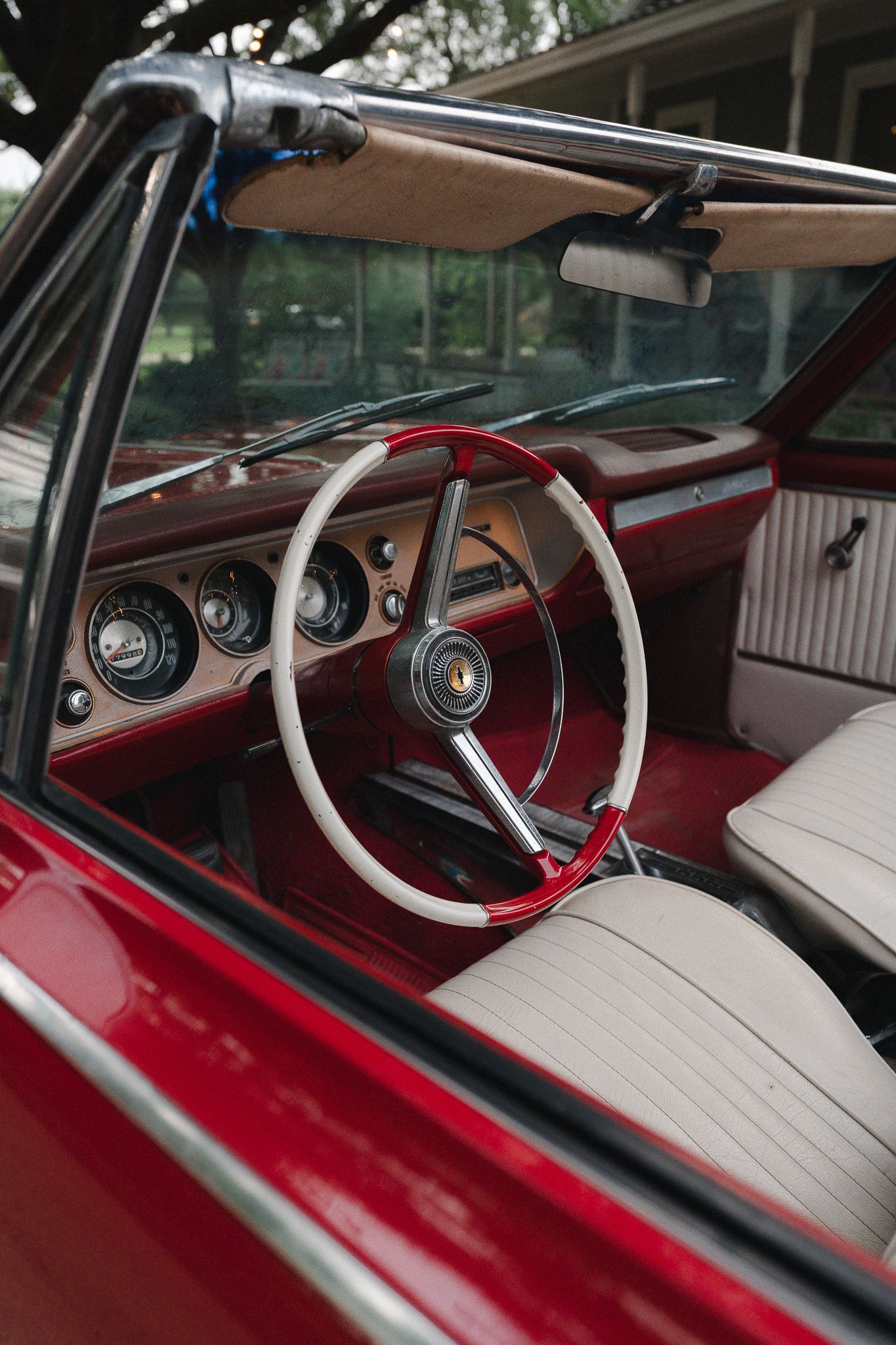 Vintage red convertible car interior featuring a white steering wheel, cream seats, and classic dashboard gauges.