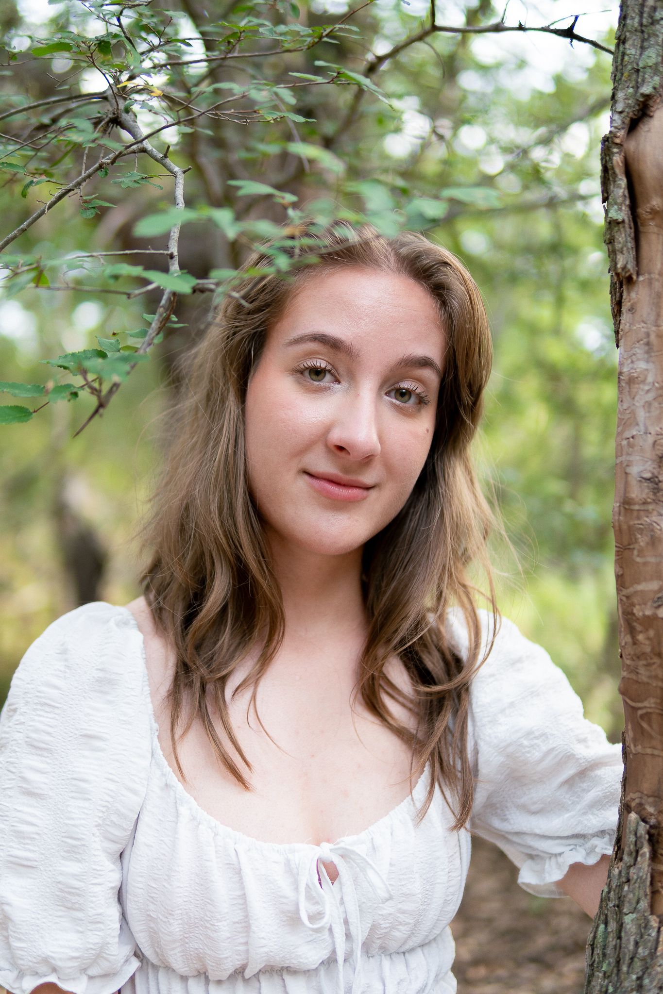 A person in a white peasant top poses among birch trees in a dreamy forest setting.