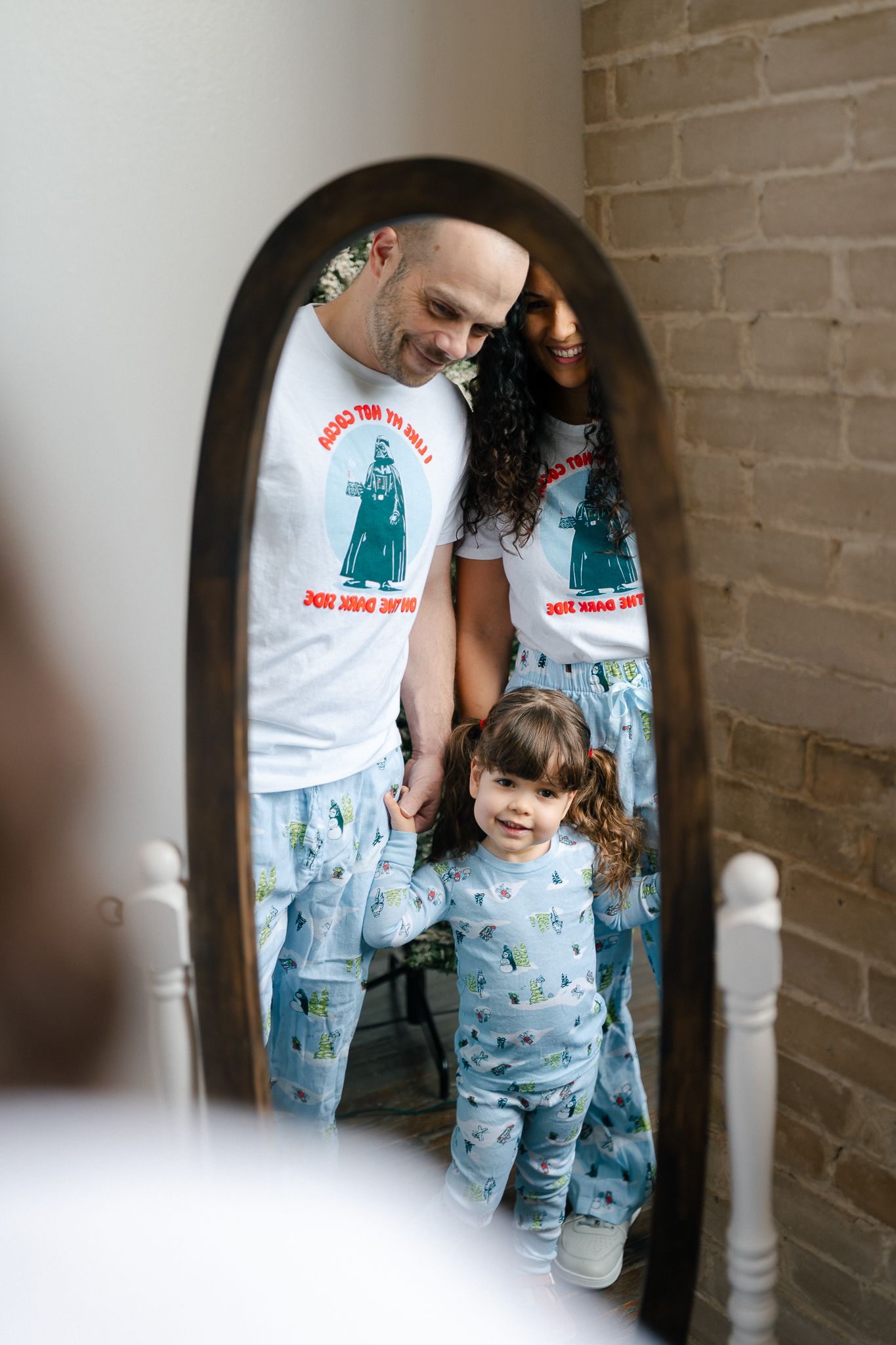 Family wearing matching pajamas poses together in a rustic hallway with exposed brick walls.