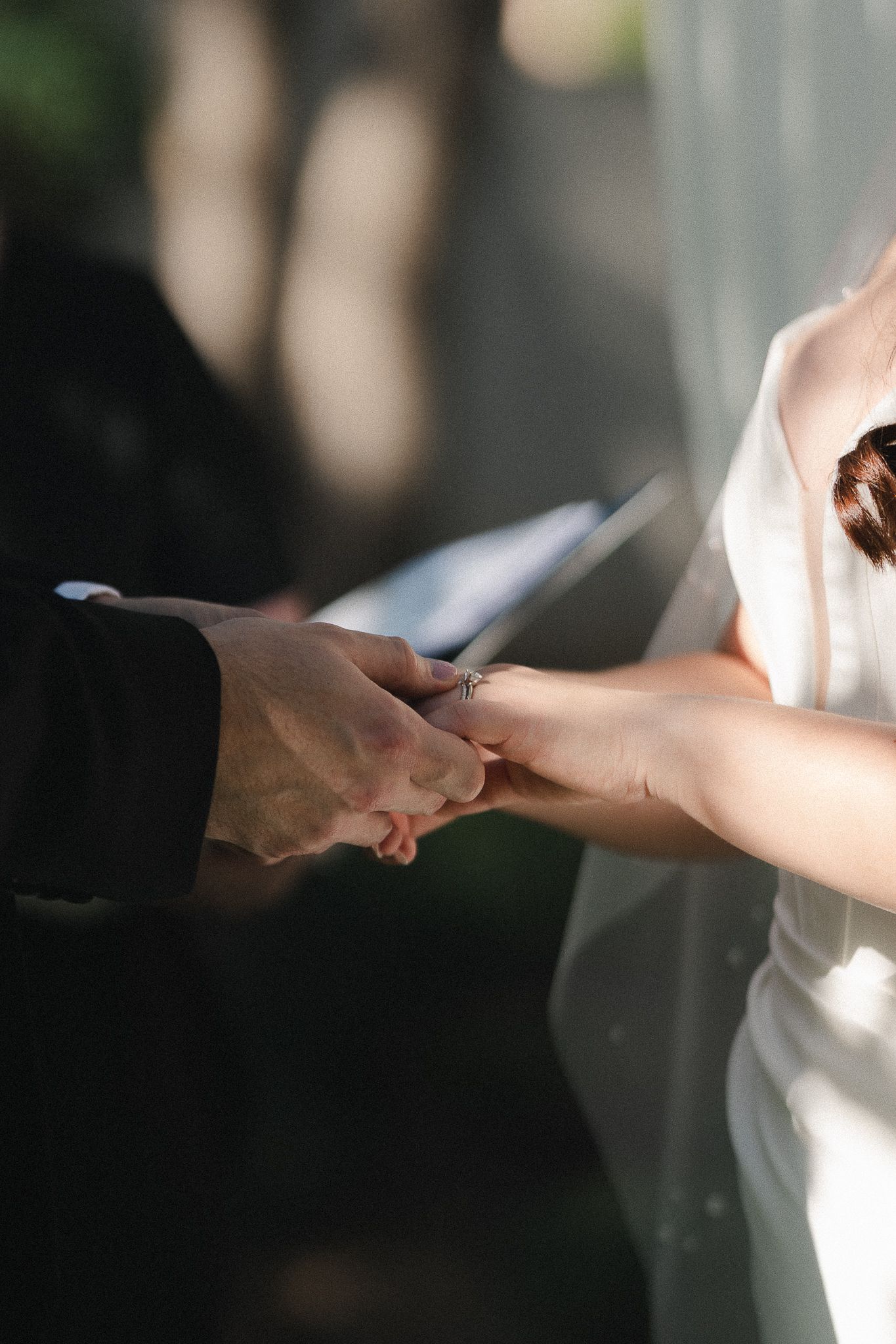 Bride and groom holding hands during wedding ring exchange ceremony, close-up of hands in elegant attire.