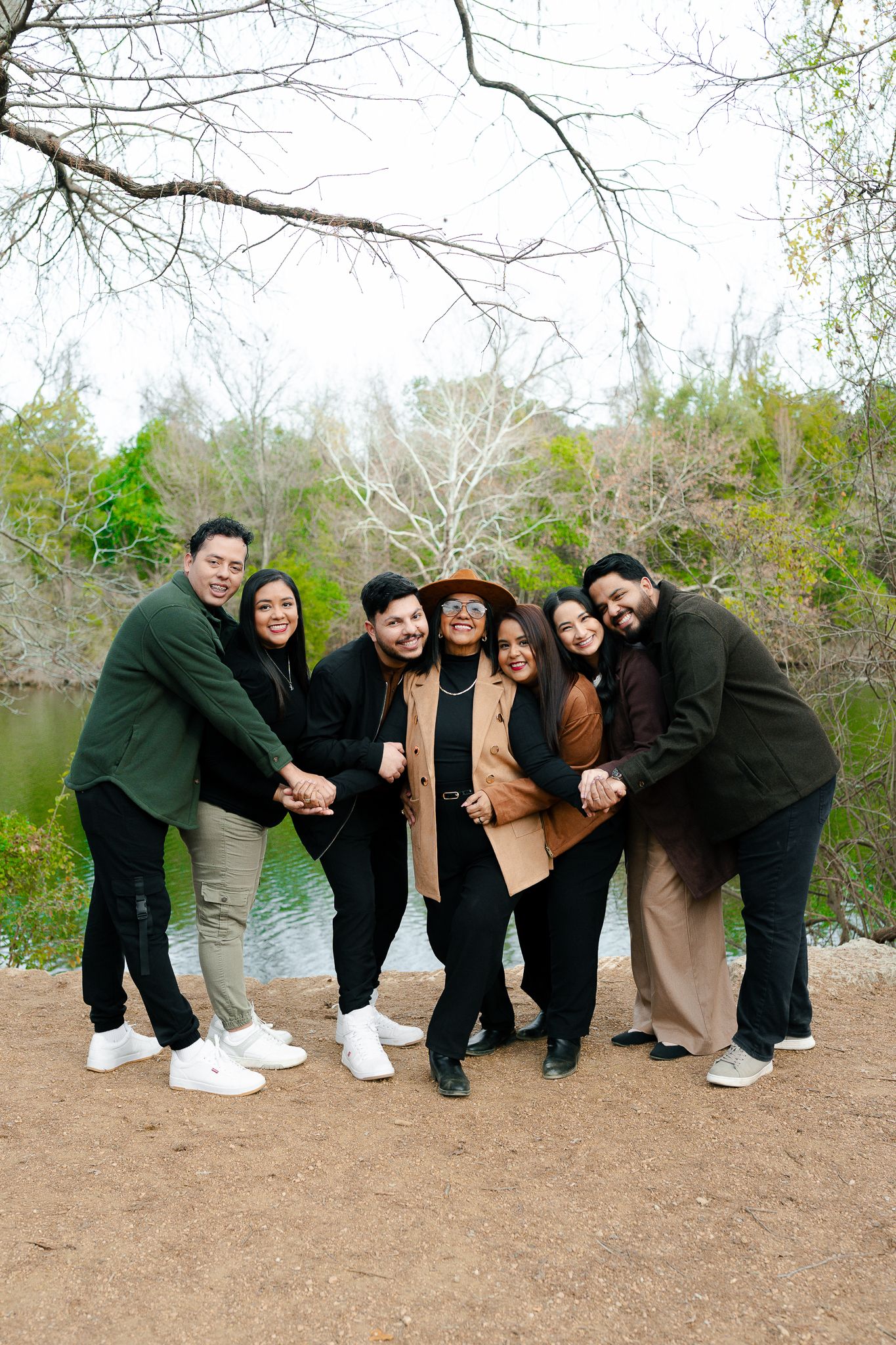 A group in coordinated black outfits poses playfully in a series of four connected photos outdoors near trees.