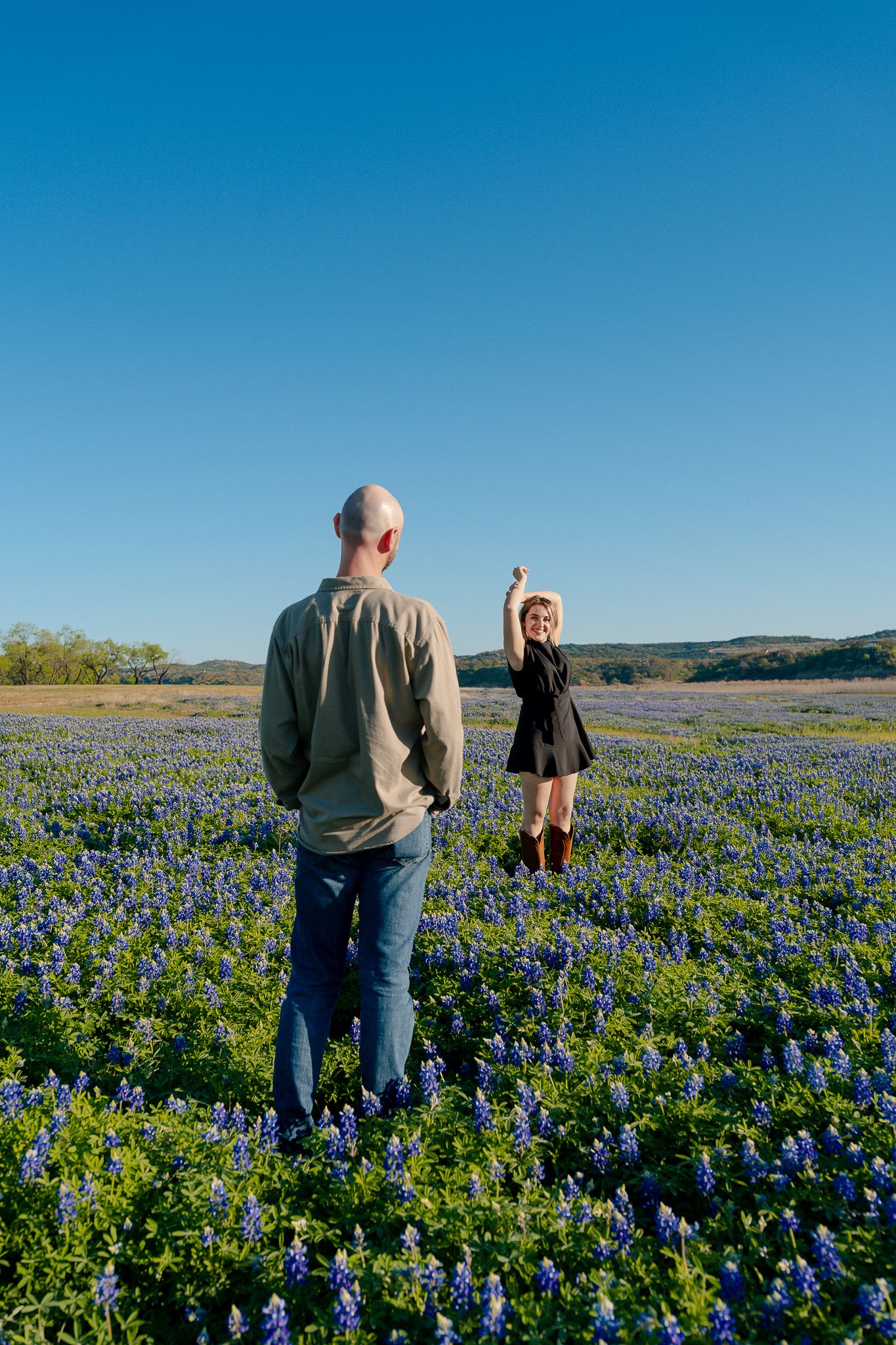 People walking through a vibrant field of blooming bluebonnets under clear blue Texas skies.