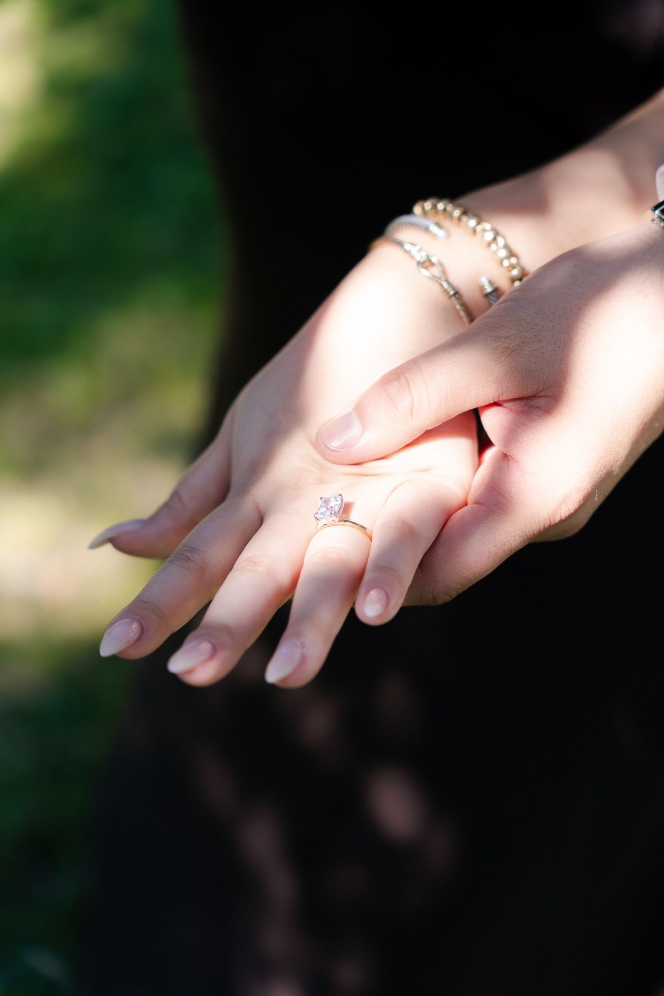 Close-up of delicate hands wearing multiple dainty gold rings against a soft blurred green background.