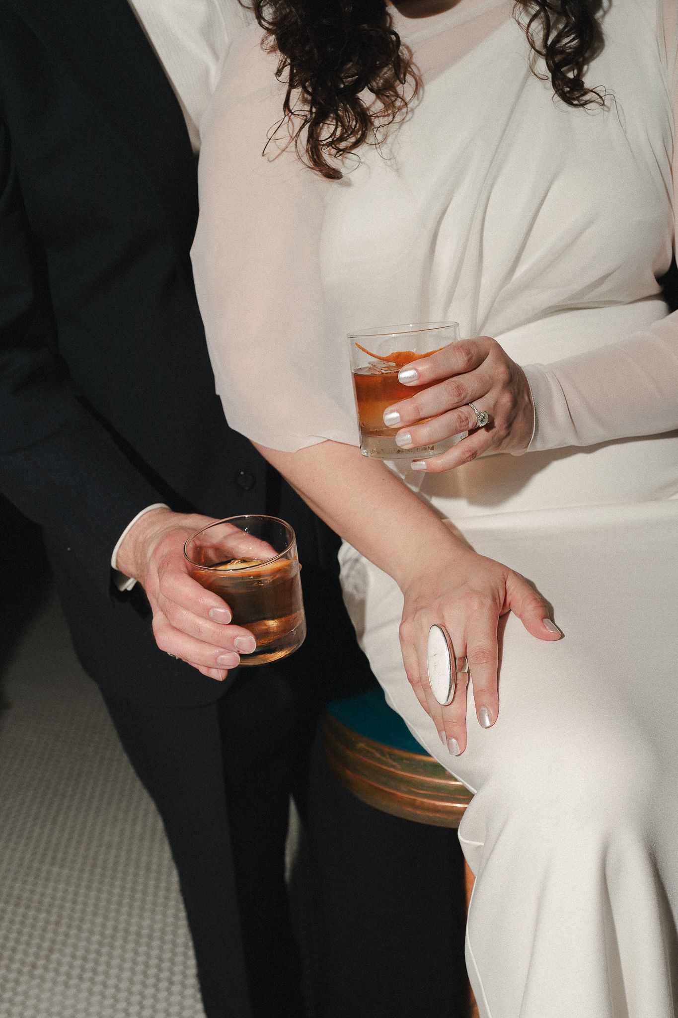 Bride and groom holding whiskey glasses, woman in white dress with ring, man in black suit at wedding reception.
