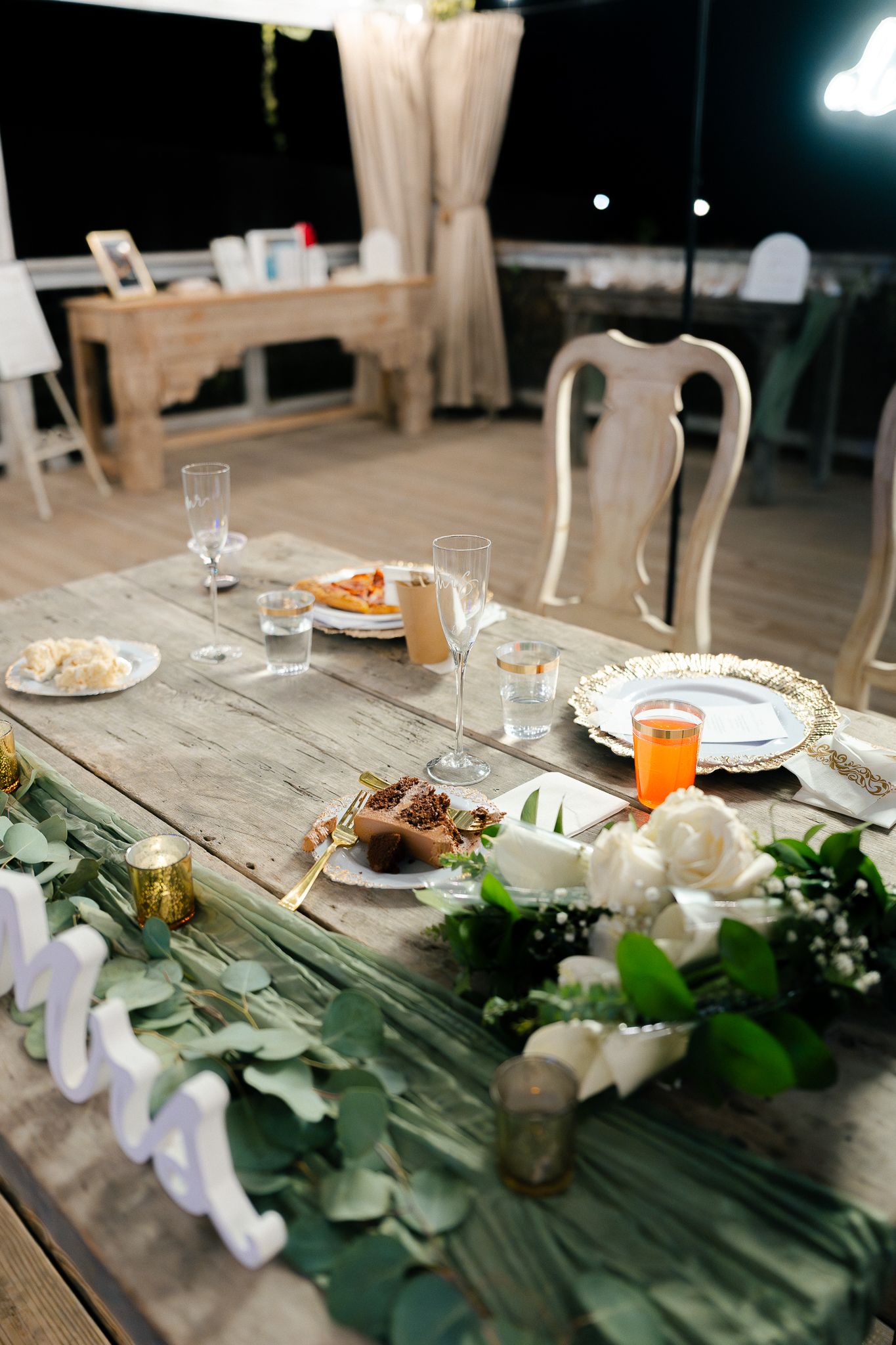 A rustic wedding reception table decorated with greenery garlands, white flowers, and place settings on weathered wood.