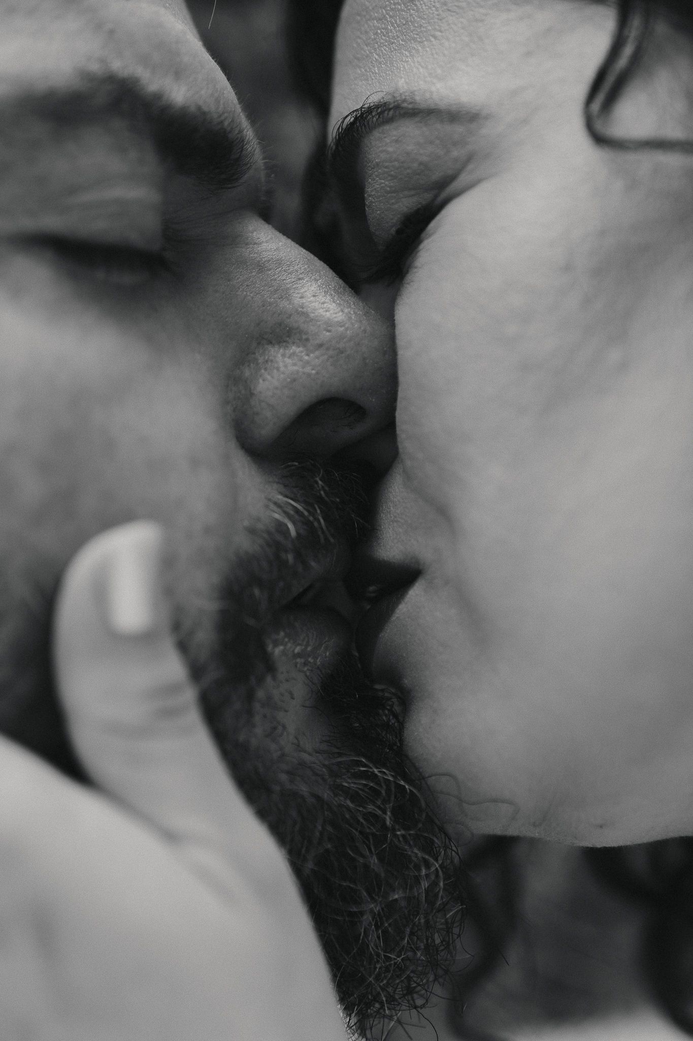 Black and white close-up photo of a couple sharing a romantic kiss, man with beard and woman with dark hair.