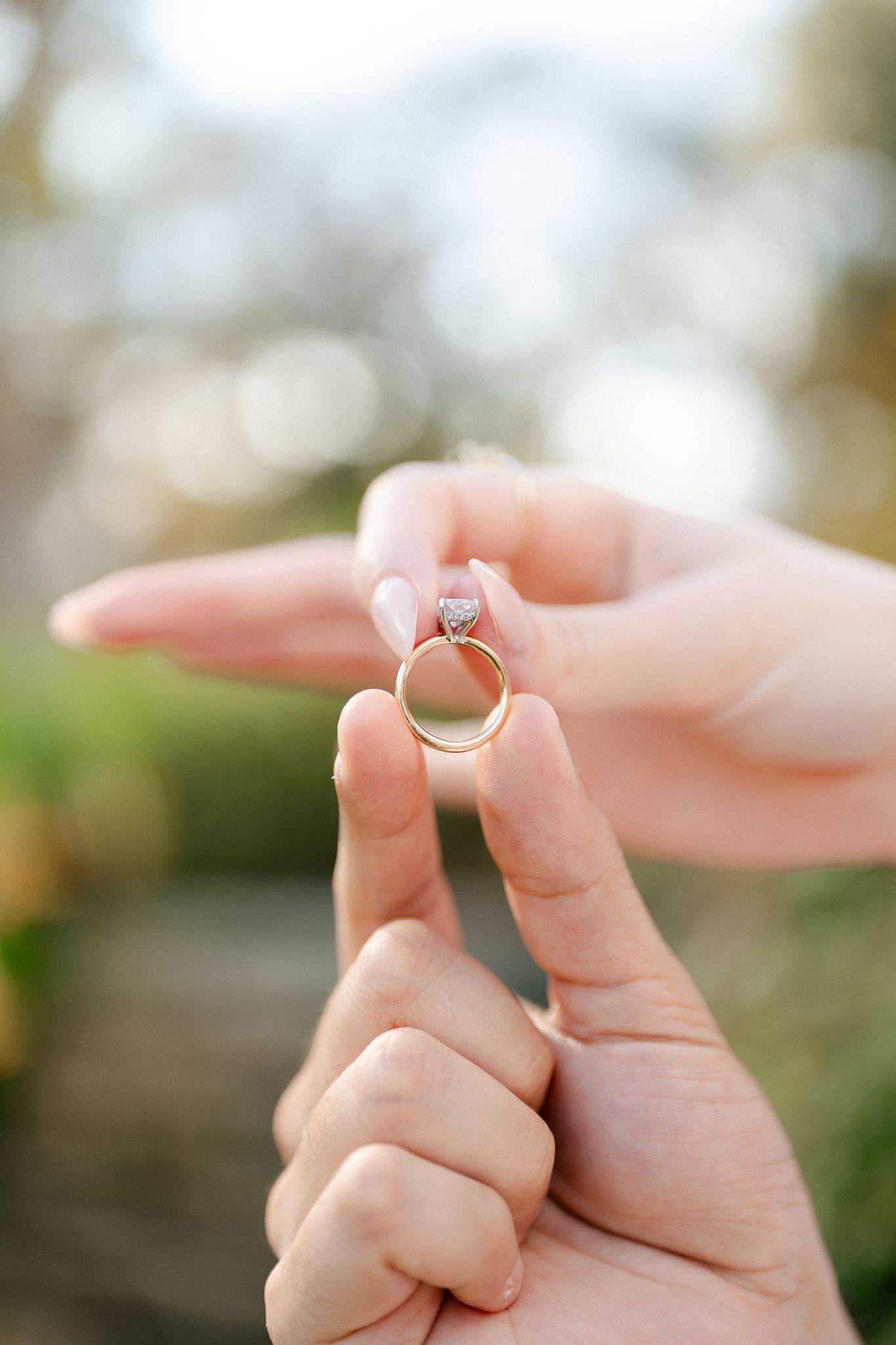 Close-up shot of hands displaying an engagement ring against a soft blurred background.