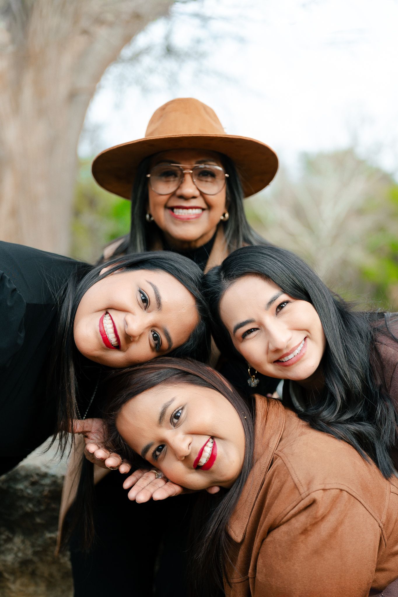 Four friends in casual attire huddle together for a joyful outdoor portrait on a bright day.
