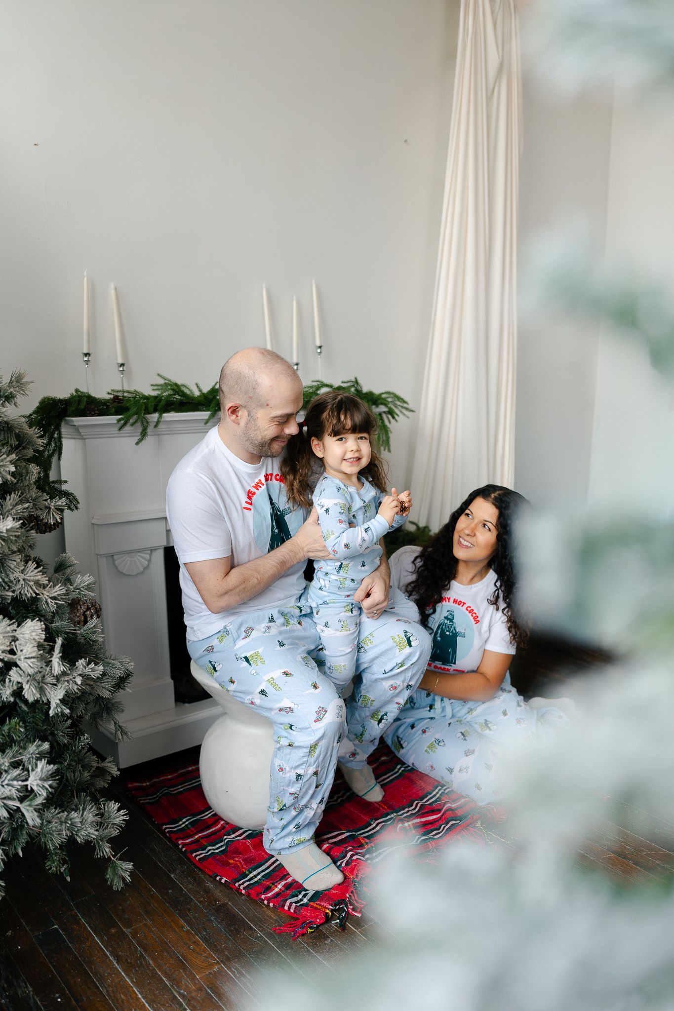 Family in matching blue pajamas sharing tender moments together on a red rug during an indoor photoshoot.