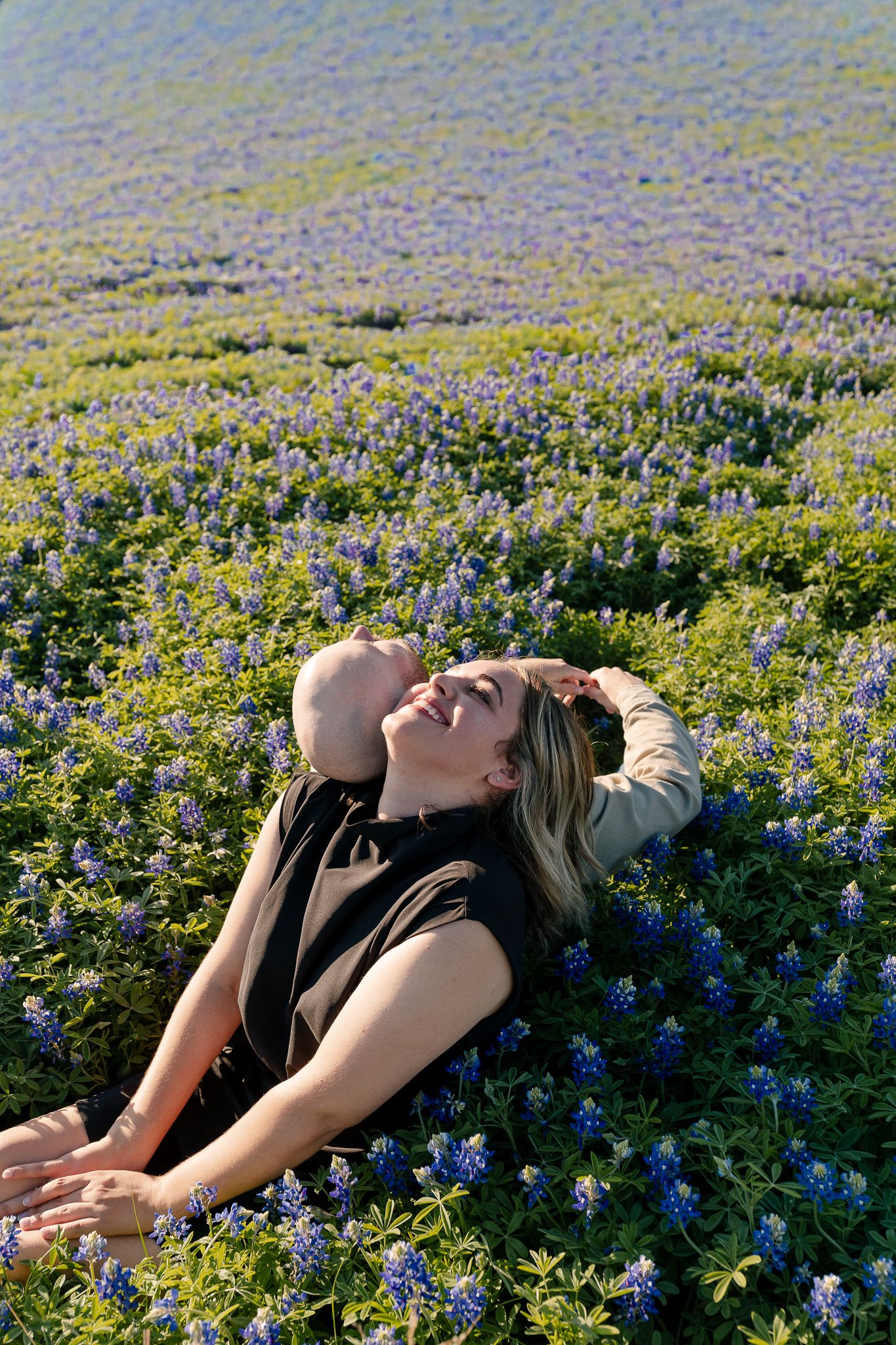 A person lying back in a field of blooming blue wildflowers on a sunny day.