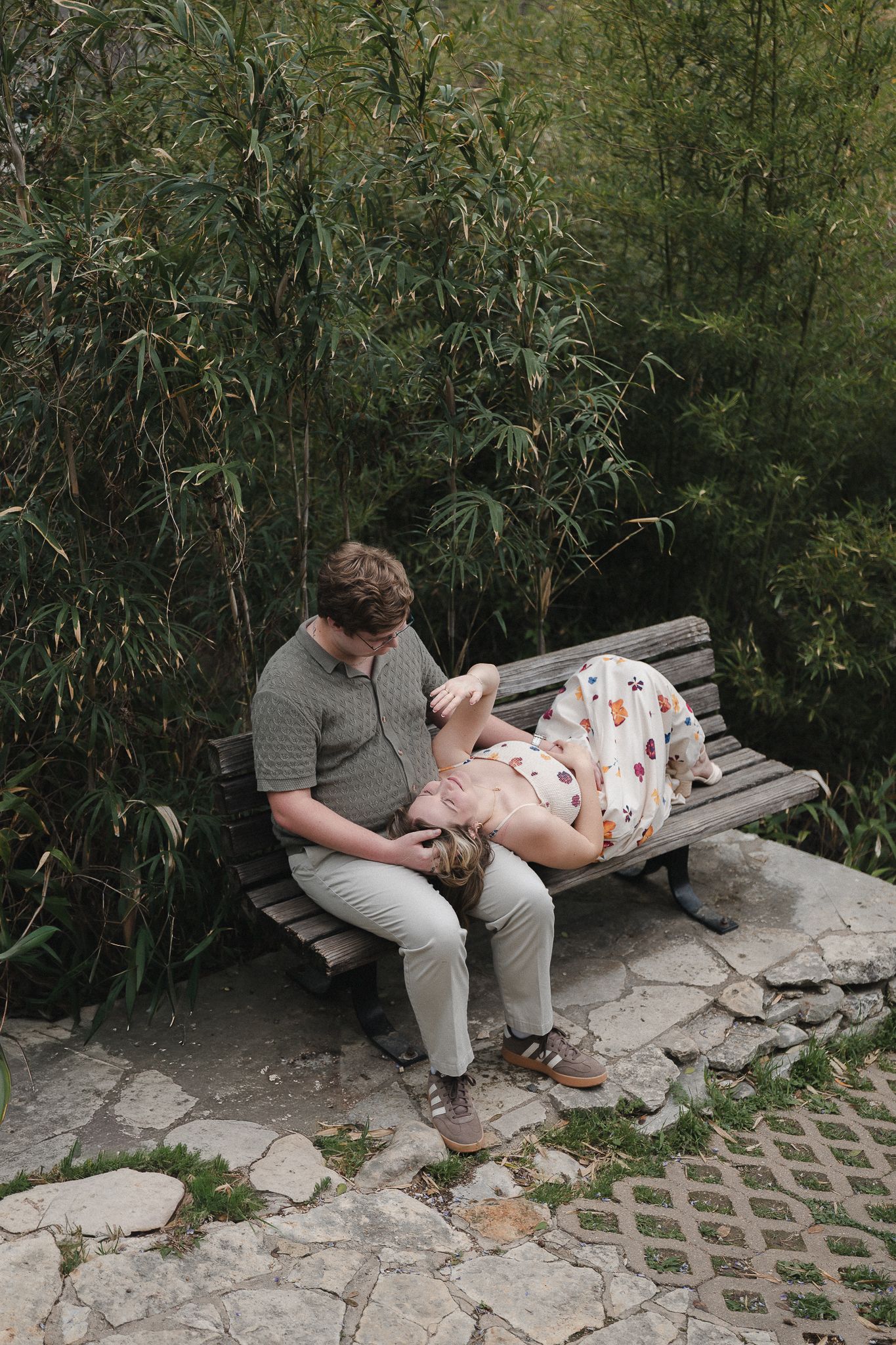 Couple relaxing on a wooden bench surrounded by bamboo in a serene garden.