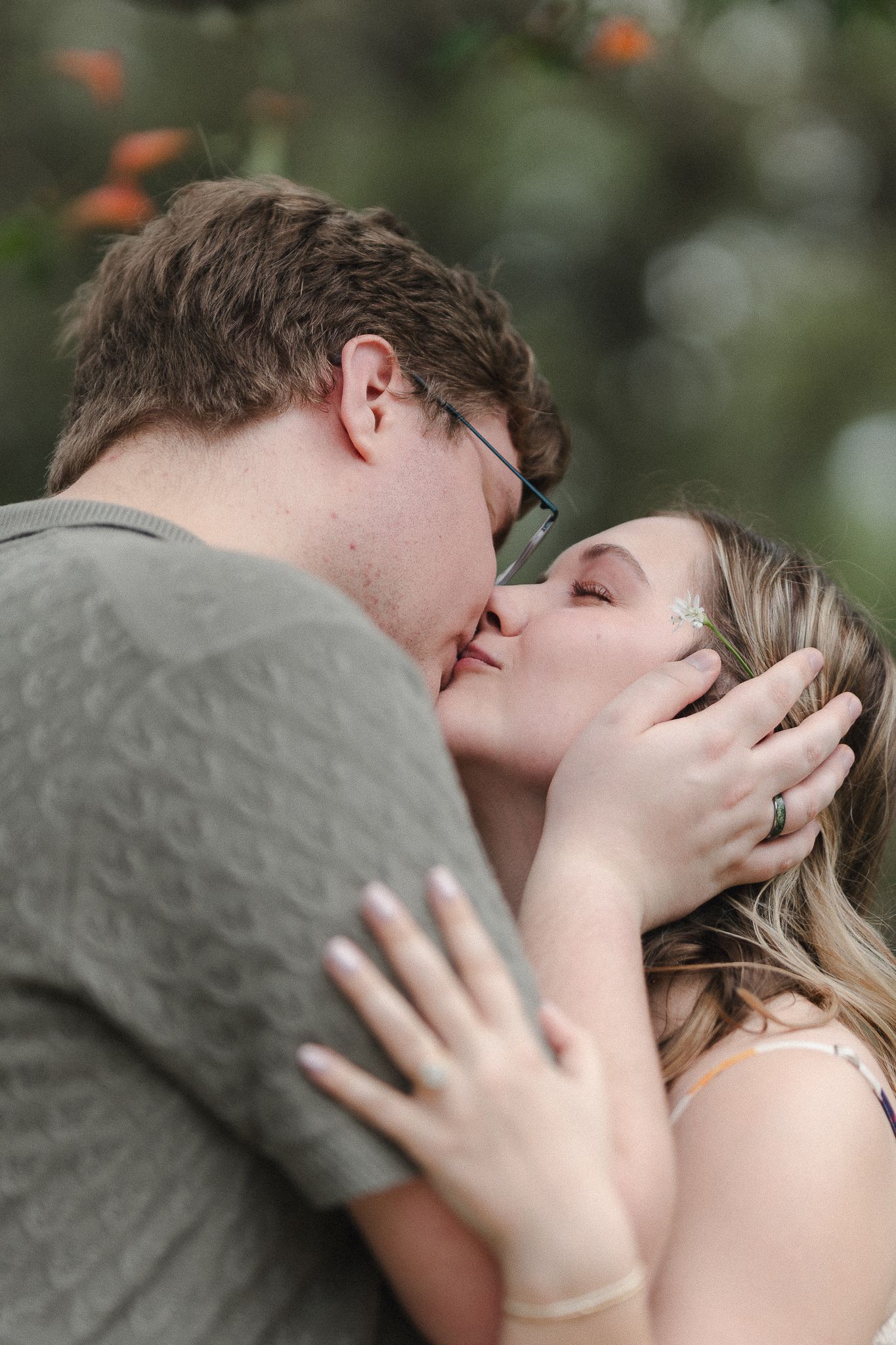 A couple shares a tender kiss outdoors, with the woman's hand gently resting on the man's chest.