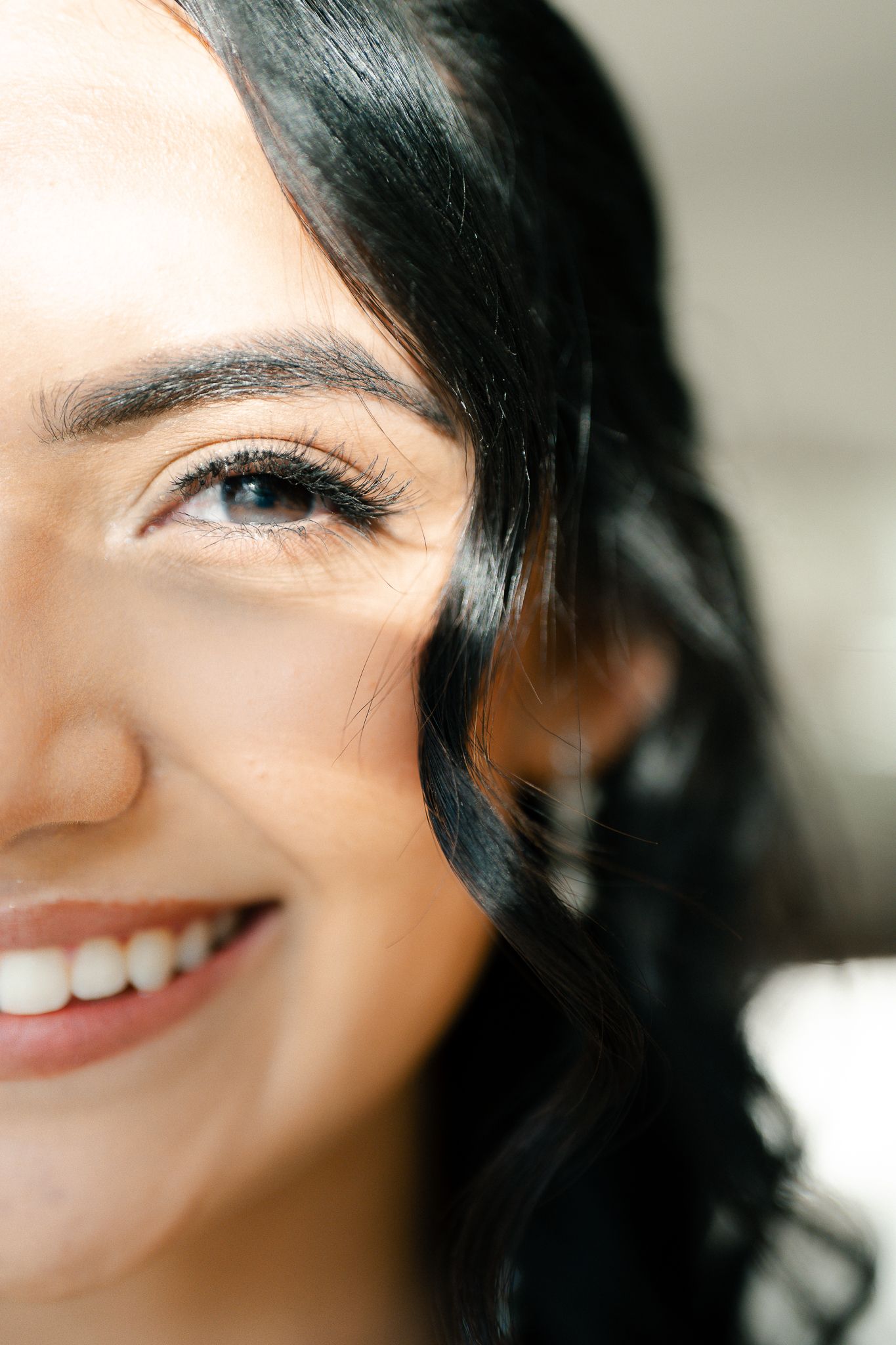 Close-up portrait showing a bright smile and dark hair against a light background.