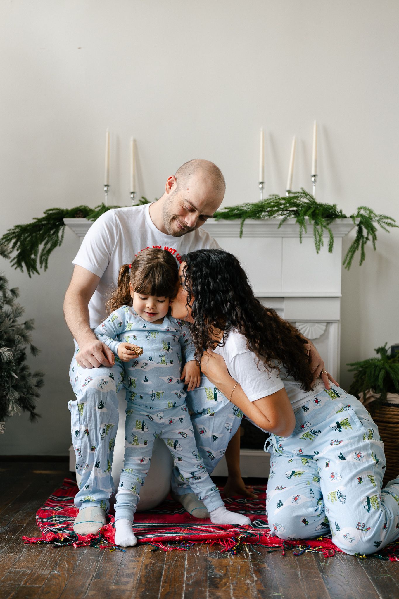 Family wearing matching holiday pajamas sits together on a red blanket for a series of candid holiday photos.