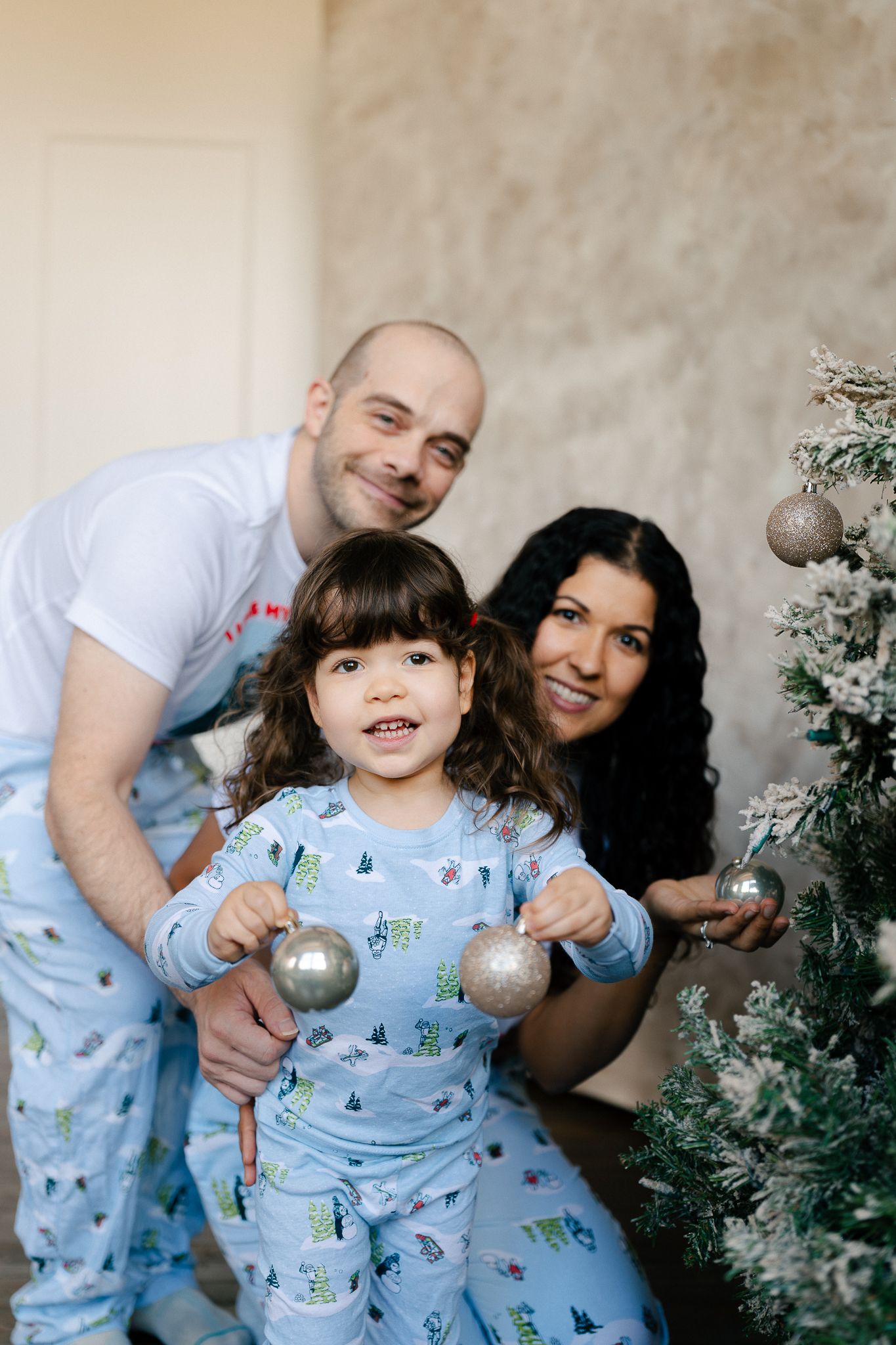 A family decorates their Christmas tree together while wearing matching blue winter-themed pajamas.