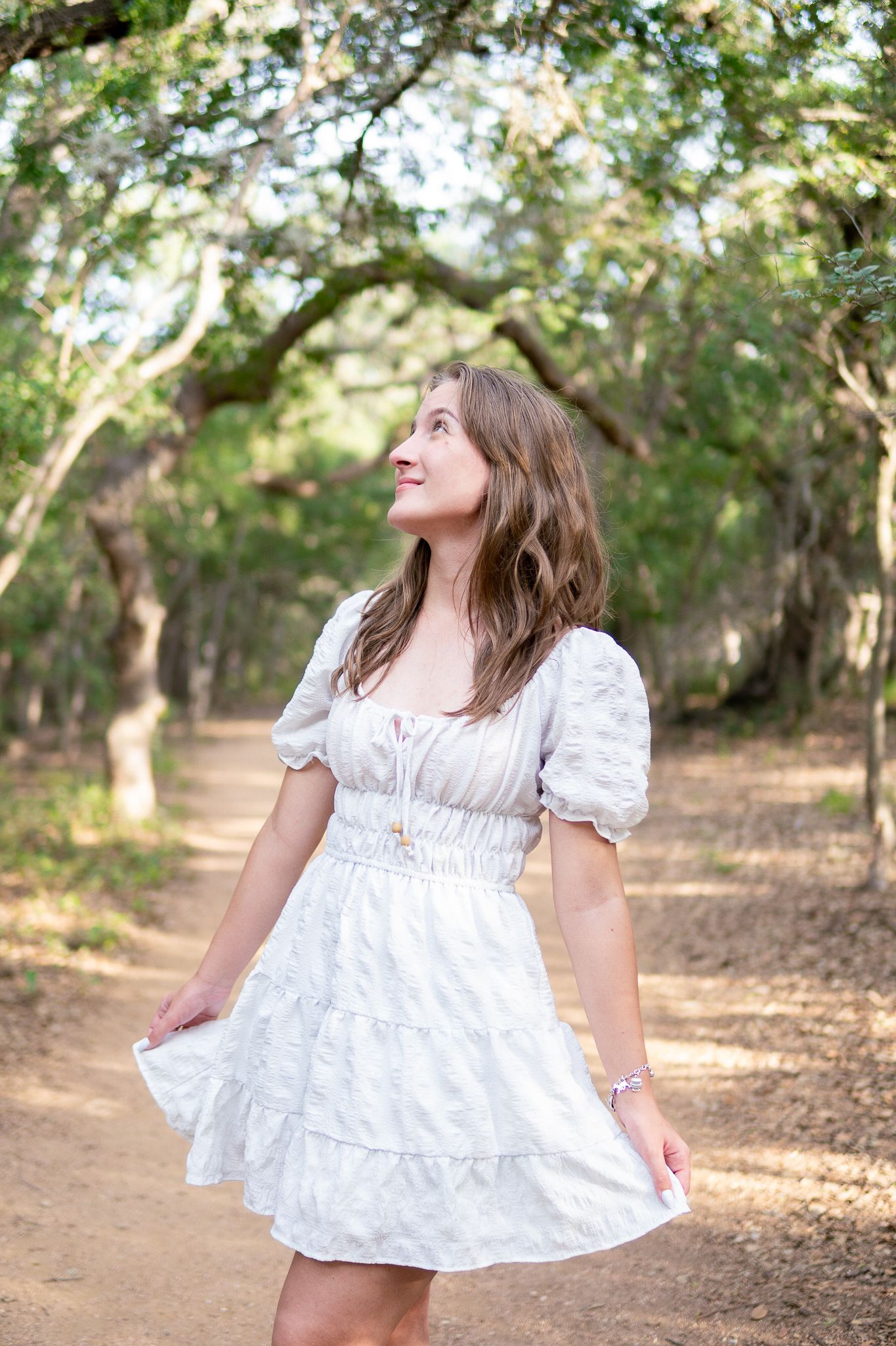 A white cotton dress twirls gracefully in a sunlit wooded area during a dreamy outdoor photoshoot.
