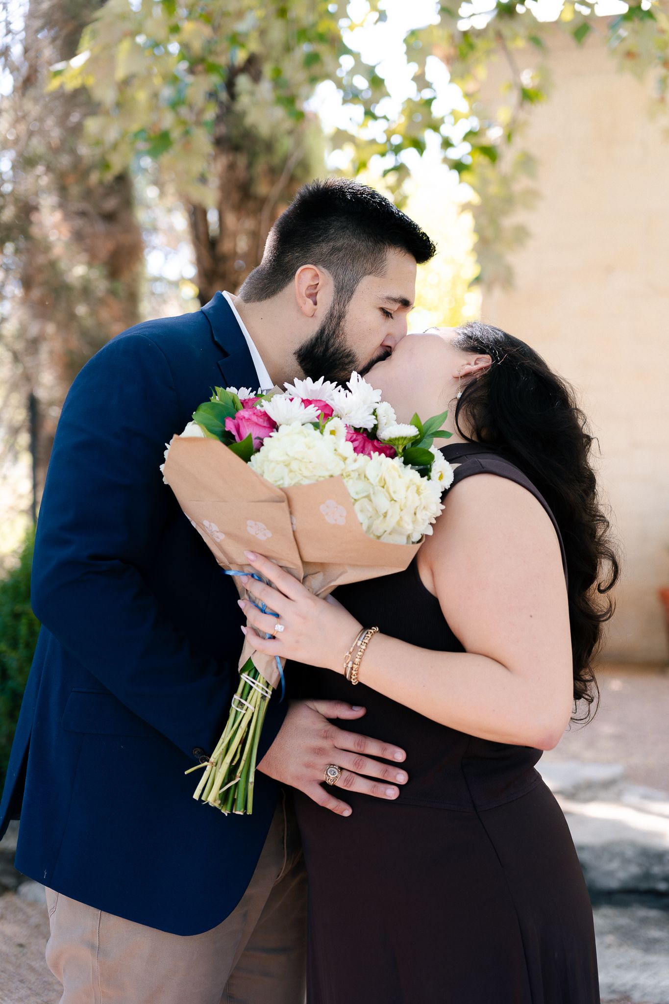 A romantic moment captured as a couple shares a kiss while holding a beautiful bouquet of white and pink flowers.