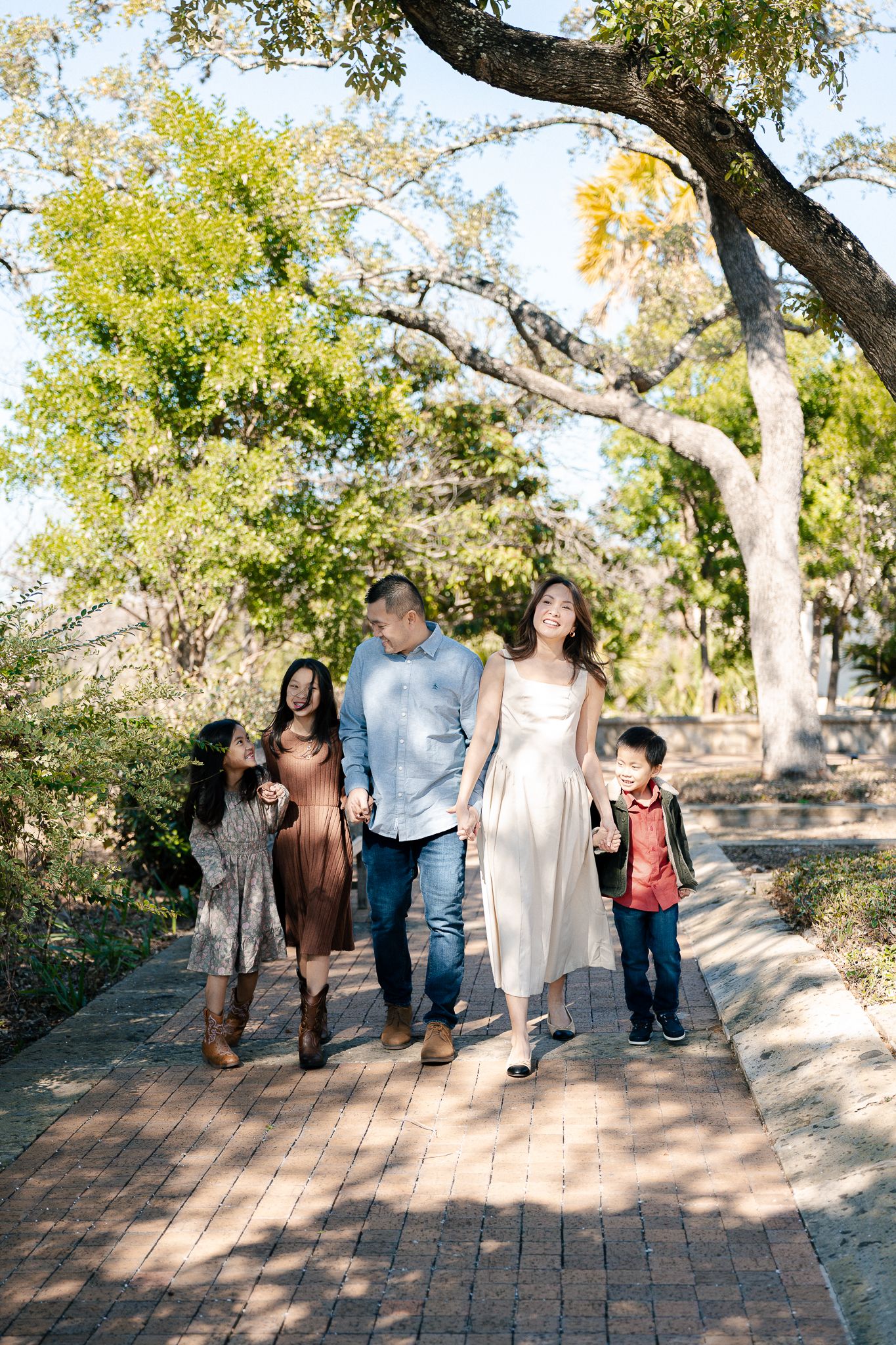 A group walks together along a winding brick path through a sunlit garden on a bright autumn day.