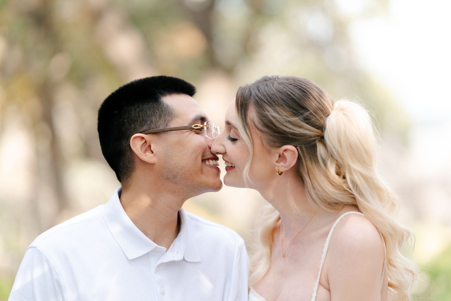 A tender moment between a couple in white clothing against a soft natural backdrop.