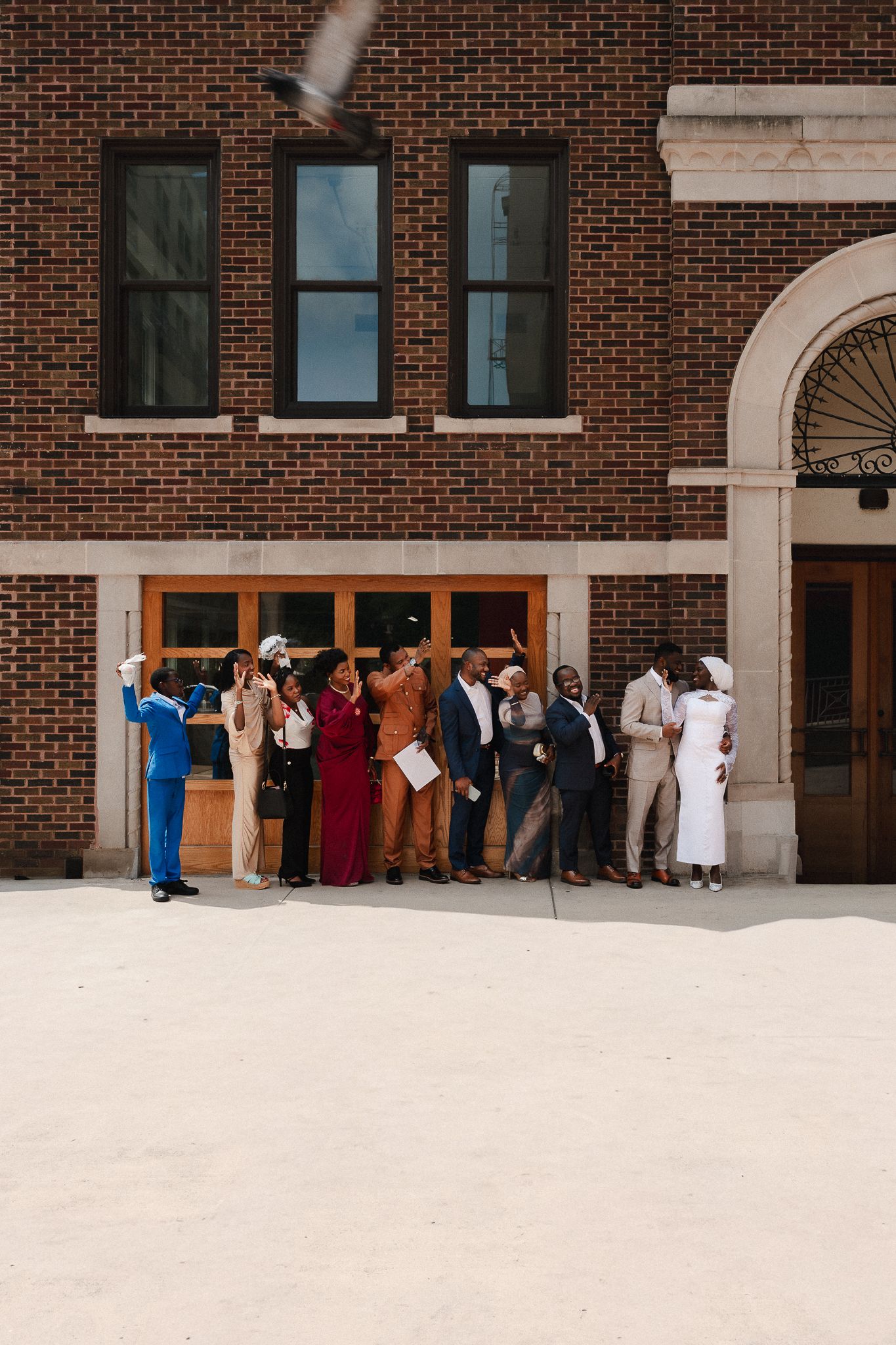 Group of elegantly dressed people posing for a photo outside a brick building during a formal celebration.