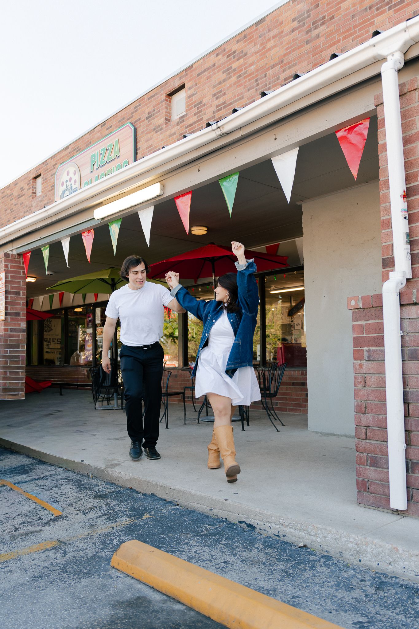 People dance and twirl under colorful triangle bunting decorations outside a brick building entrance.