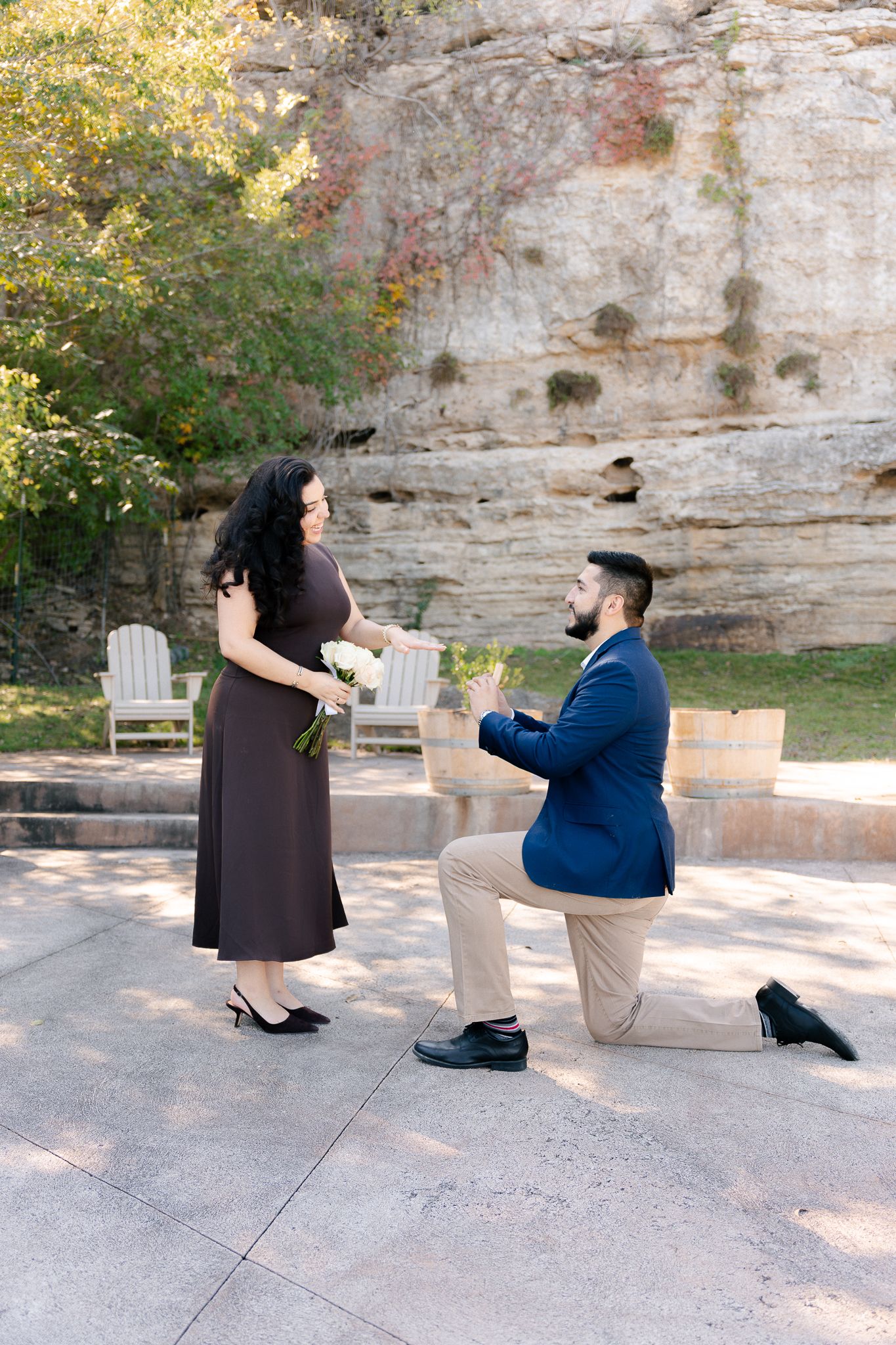 A romantic proposal sequence showing a couple by a stone wall as one partner gets down on one knee to propose.