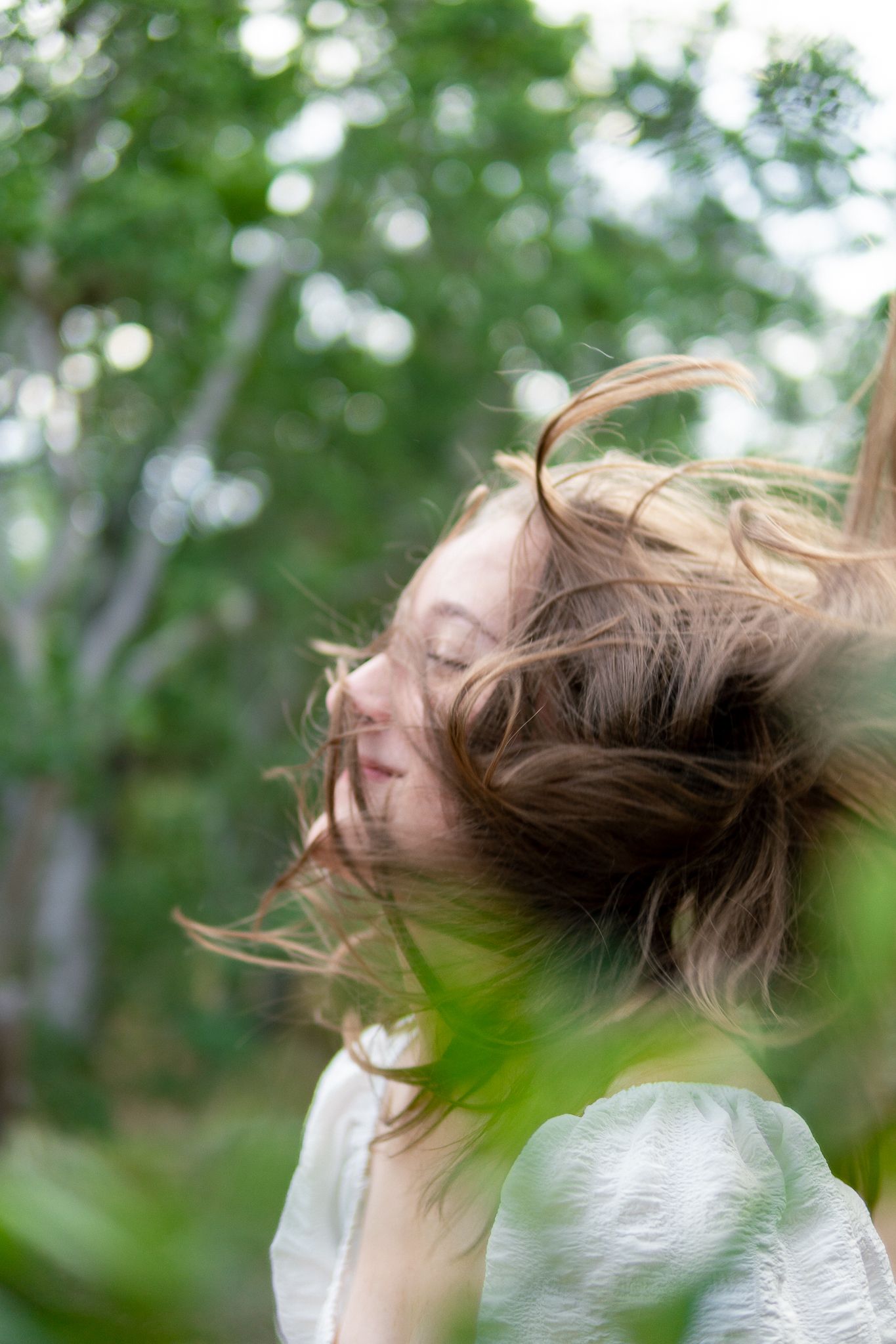 A sequence of motion shots showing long hair flowing dramatically in the wind against a blurred green outdoor background.