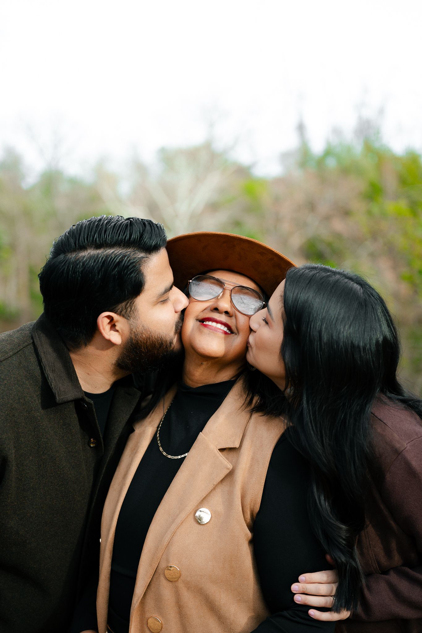 A heartwarming family moment captured outdoors as three people share loving kisses and embraces while wearing fall attire.