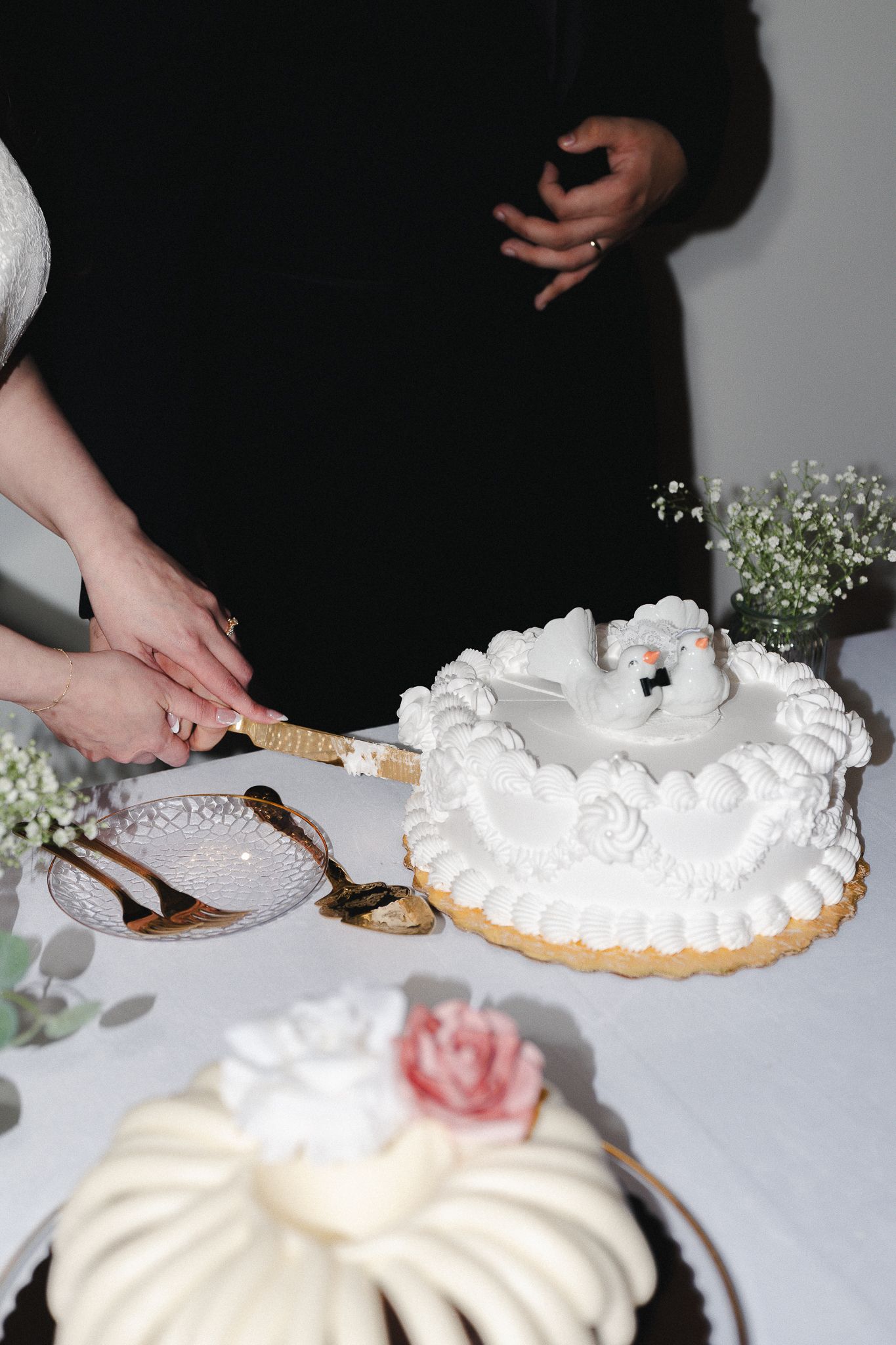 Couple cutting a white wedding cake decorated with swan toppers and floral details at a reception table.