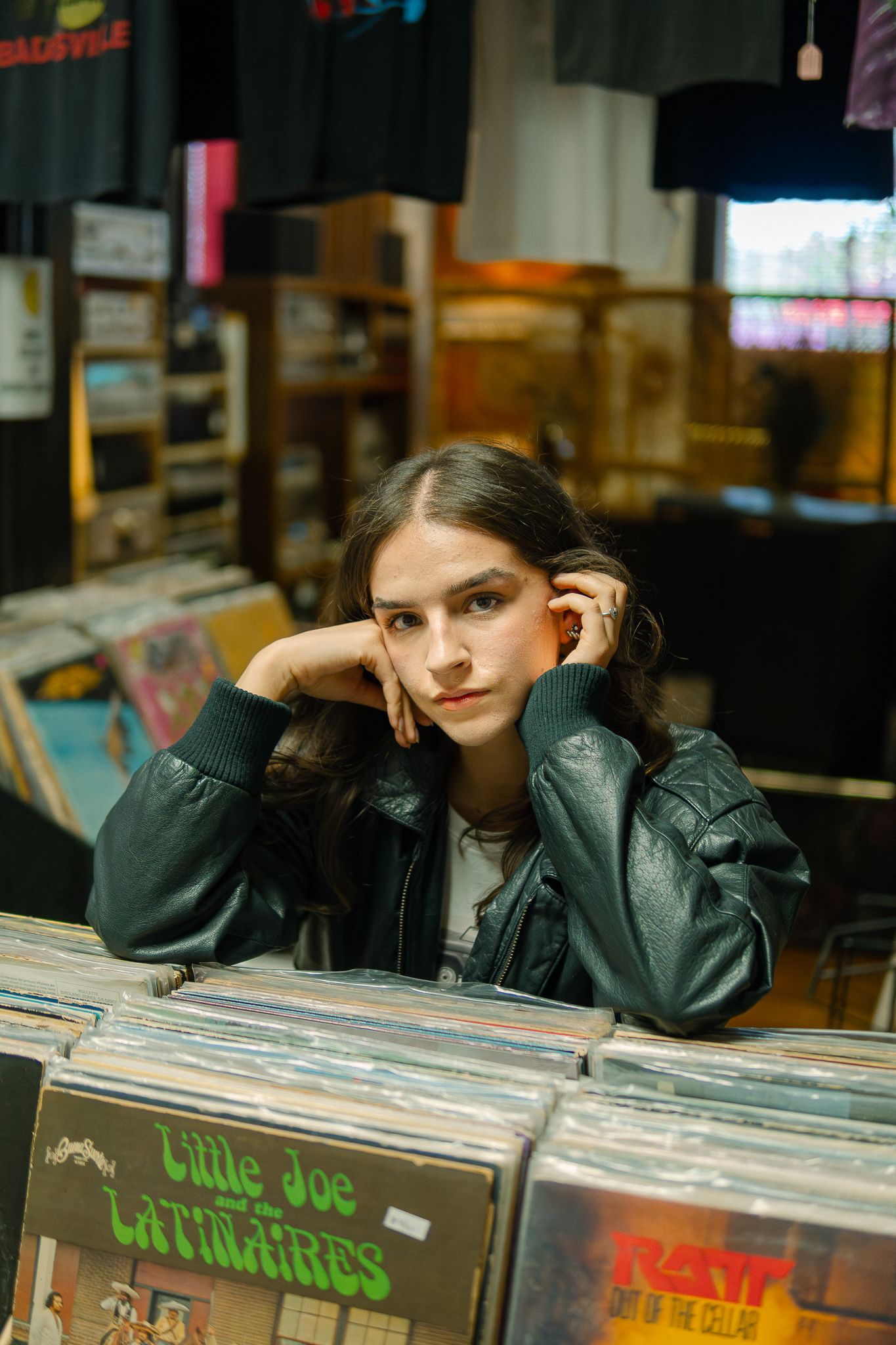 Person in black leather jacket browses through vinyl records at a record store.