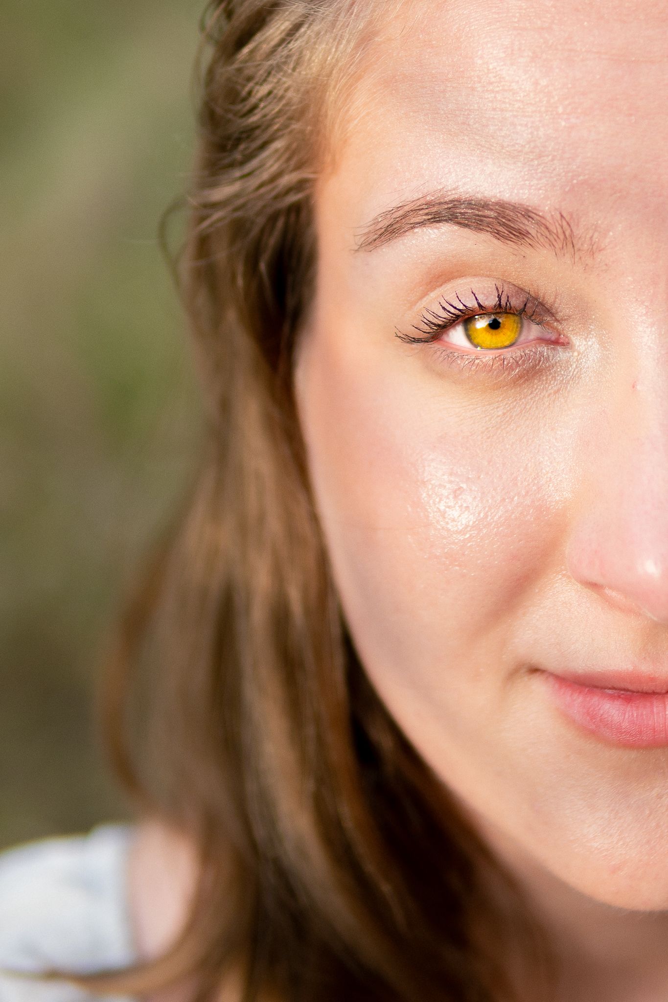A close-up portrait showing bright yellow contact lenses against fair skin and long eyelashes.