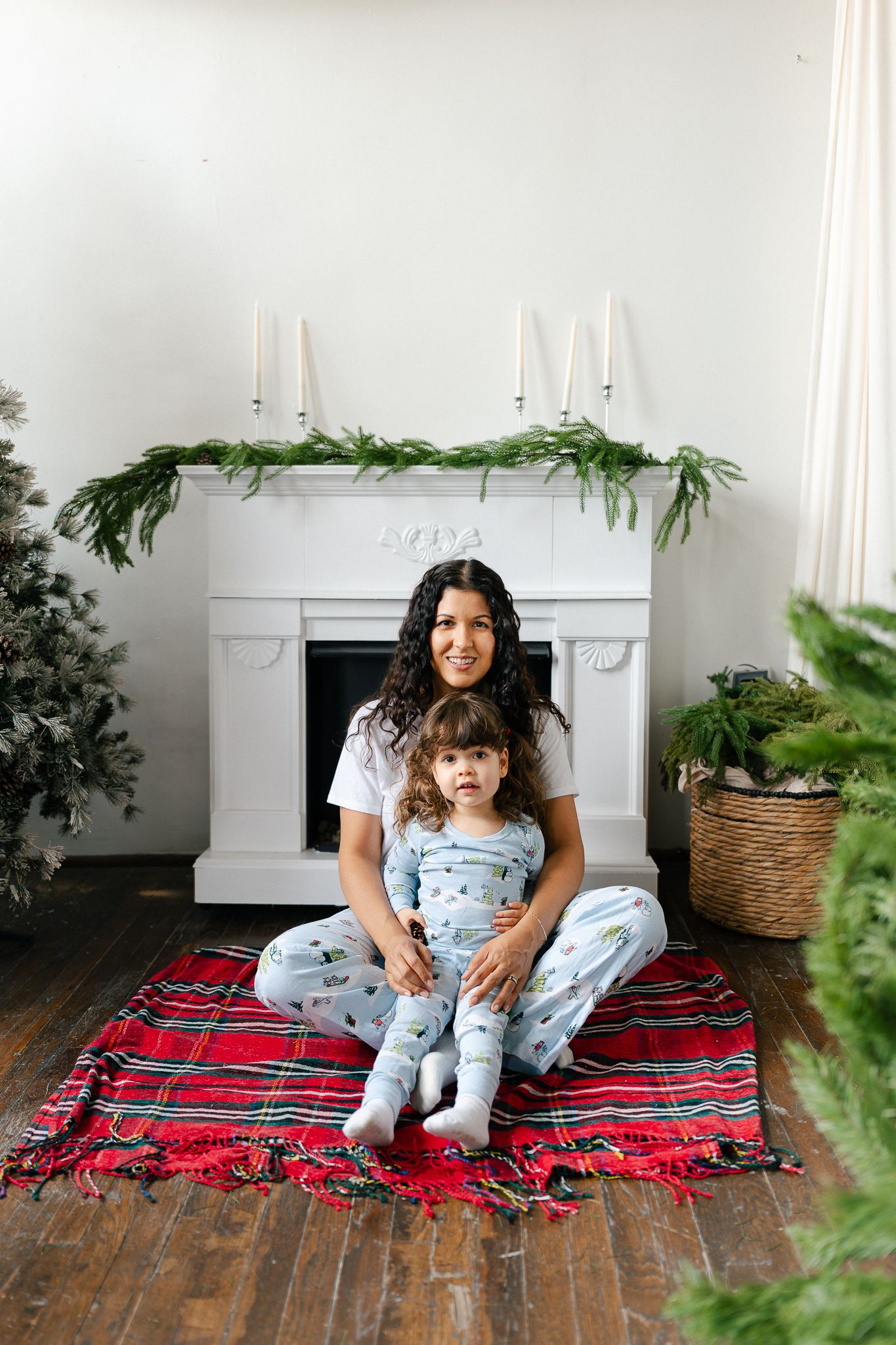 A cozy indoor scene with a red plaid blanket, white fireplace mantel, and decorative greenery in woven baskets.