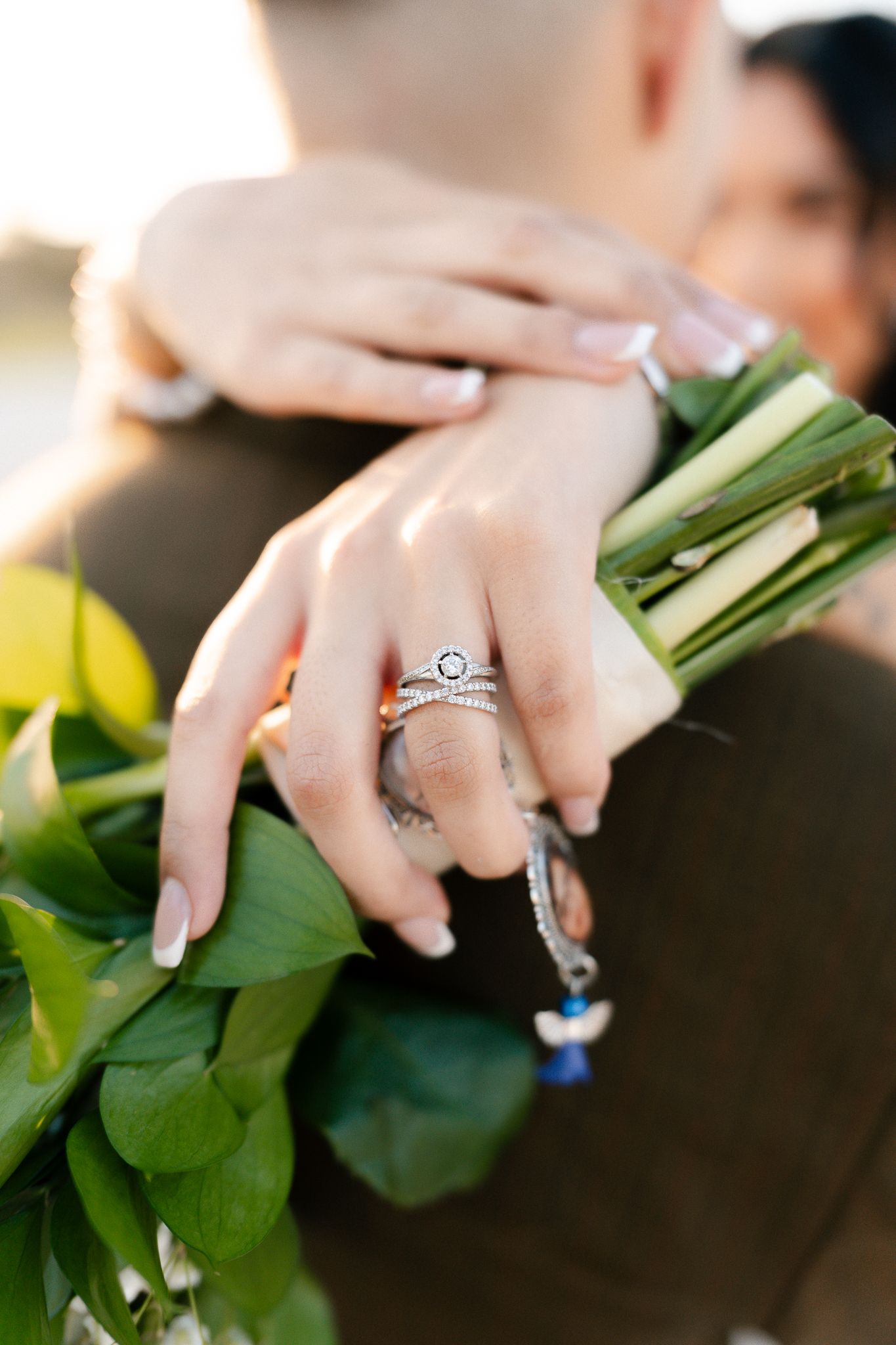 Close-up of hands holding a bouquet showing an elegant engagement ring with a round center stone.