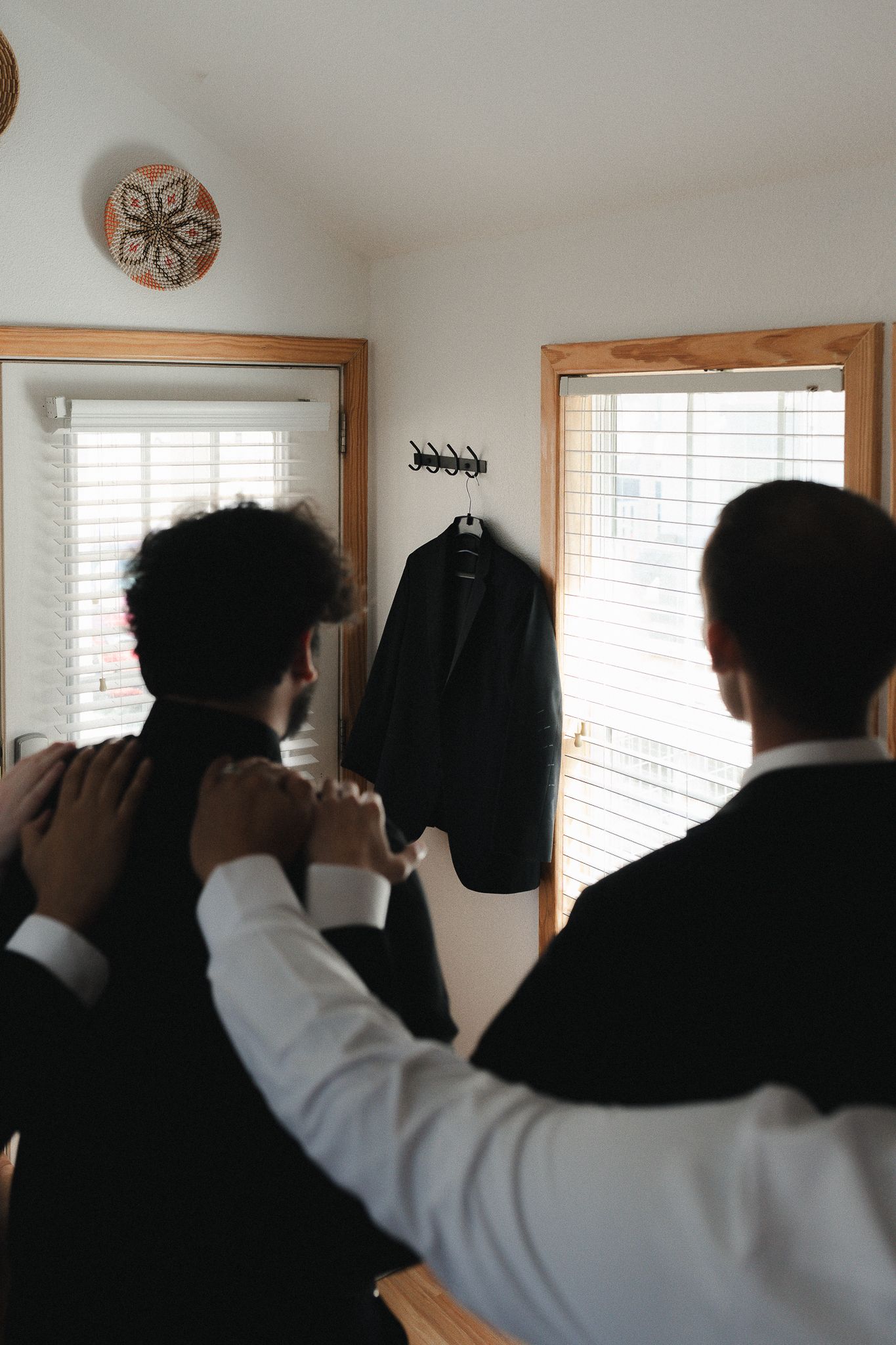 Groomsmen helping each other get dressed in black tuxedos before a wedding ceremony indoors.