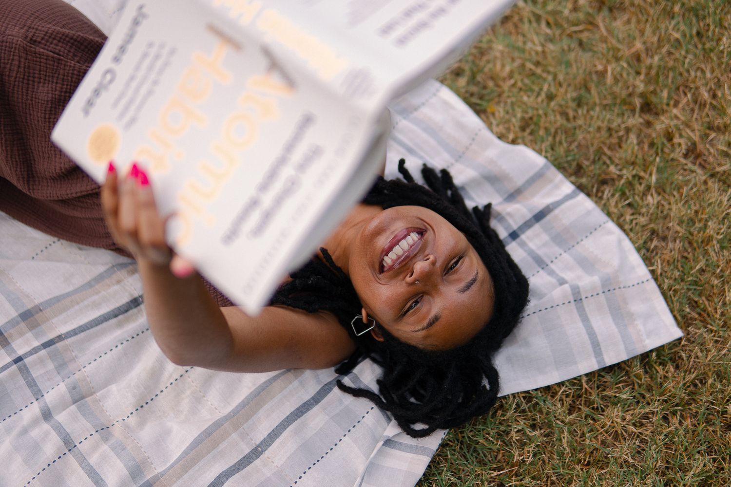 A person lies on grass while reading a book outdoors on a sunny day.