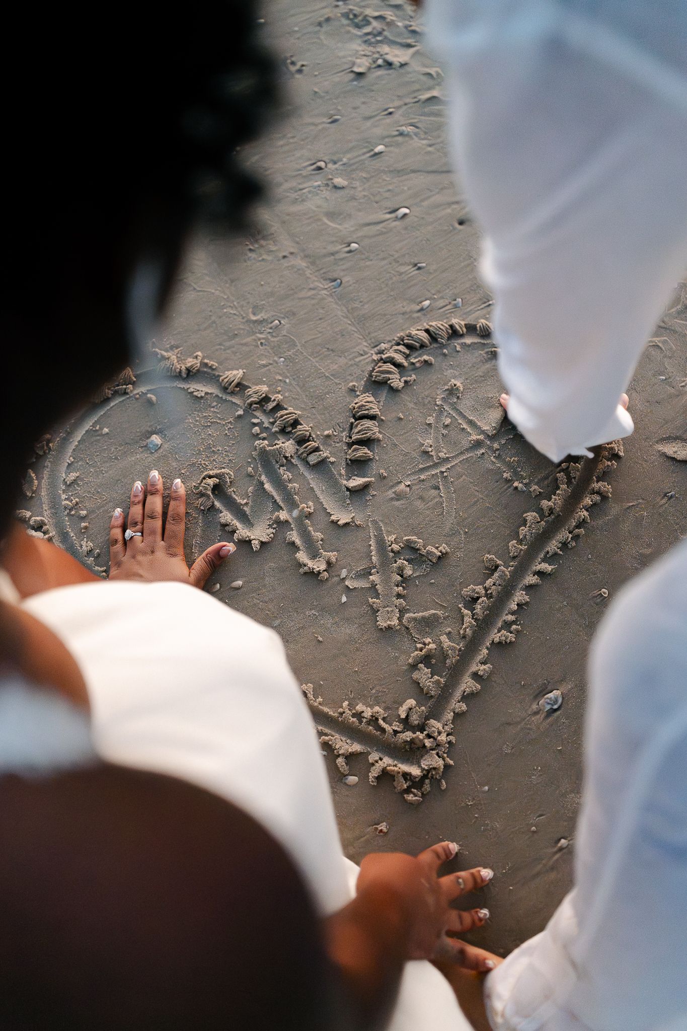 Small hands write messages in sand on a beach during a sunny day.