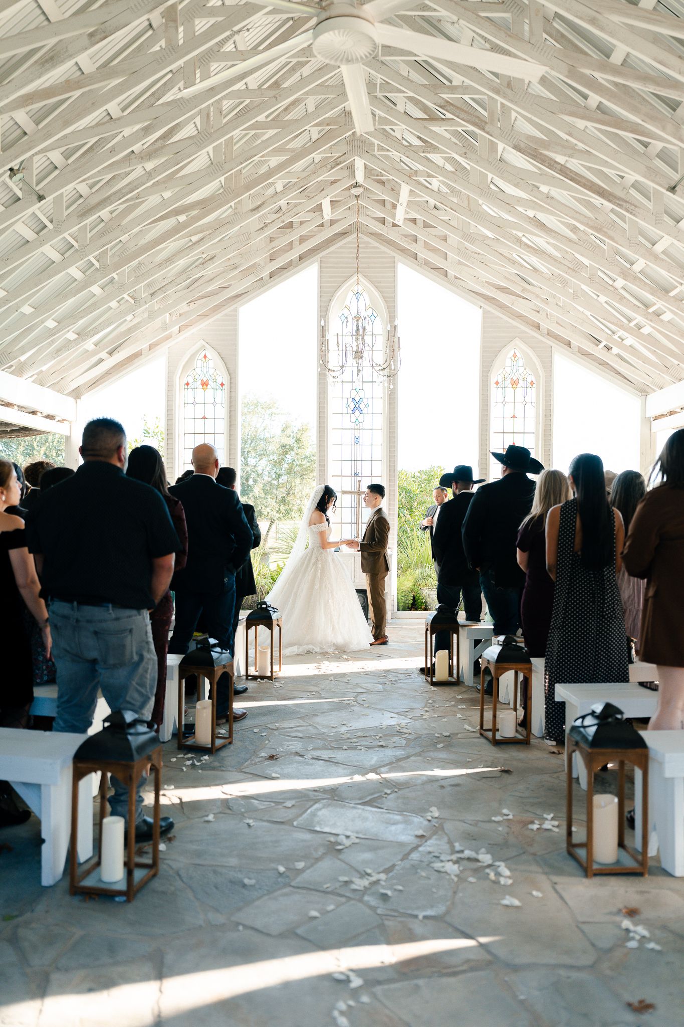 People seated in rows inside a bright white chapel with exposed wooden beams during a ceremony.