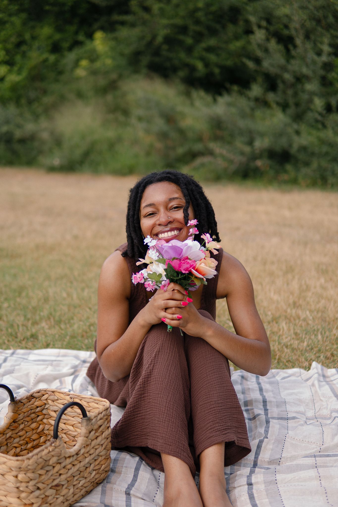 A joyful person relaxes on a picnic blanket while holding a vibrant bouquet of pink and purple flowers.