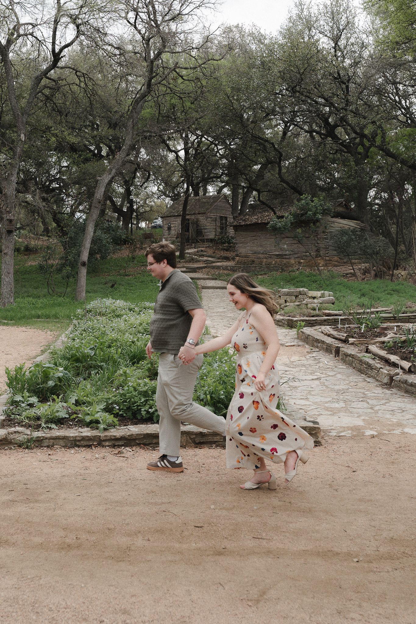 A couple joyfully runs hand-in-hand through a rustic garden path surrounded by trees and stone steps.