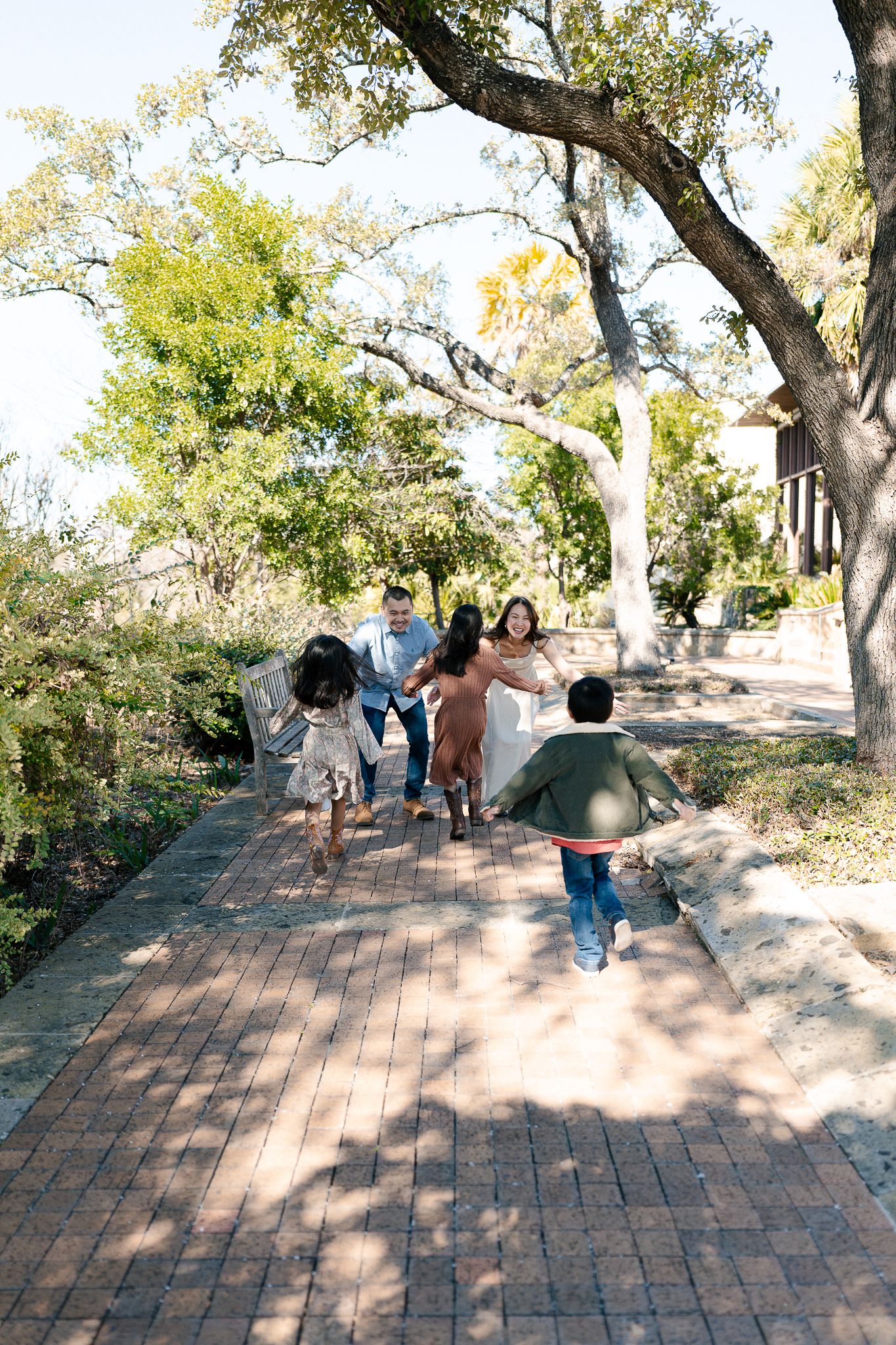 People walk along a brick path surrounded by trees and greenery in an outdoor park setting.