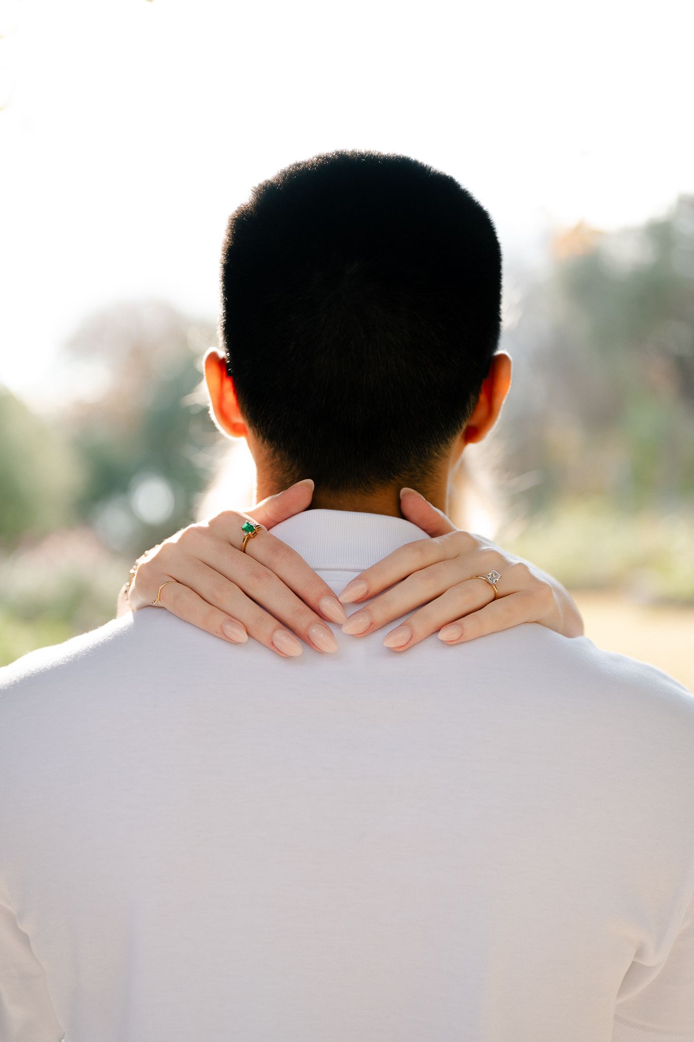 Close-up view of hands gently resting on the back of a neck while wearing a white shirt in soft natural lighting.