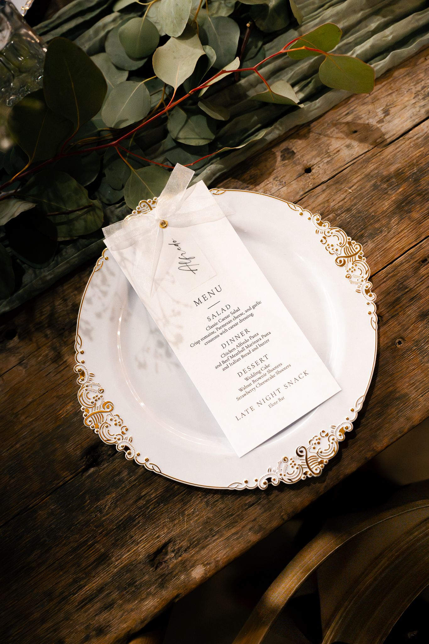Elegant white paper doilies with gold edges display wedding menu cards on a rustic wooden surface with eucalyptus leaves.