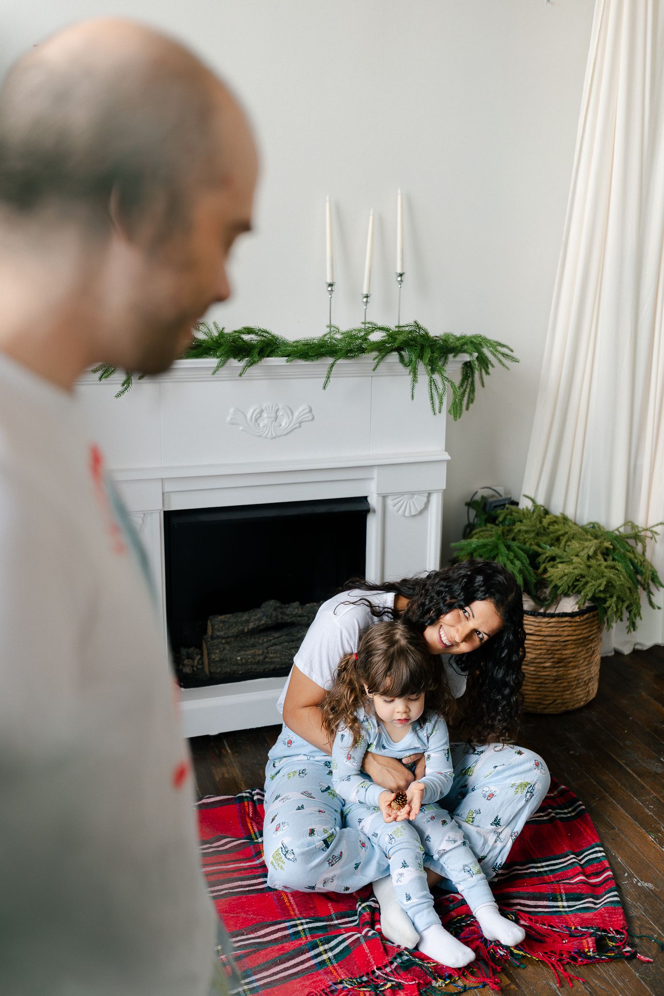 Two people in matching blue pajamas sit together on a red and black striped blanket near a fireplace.