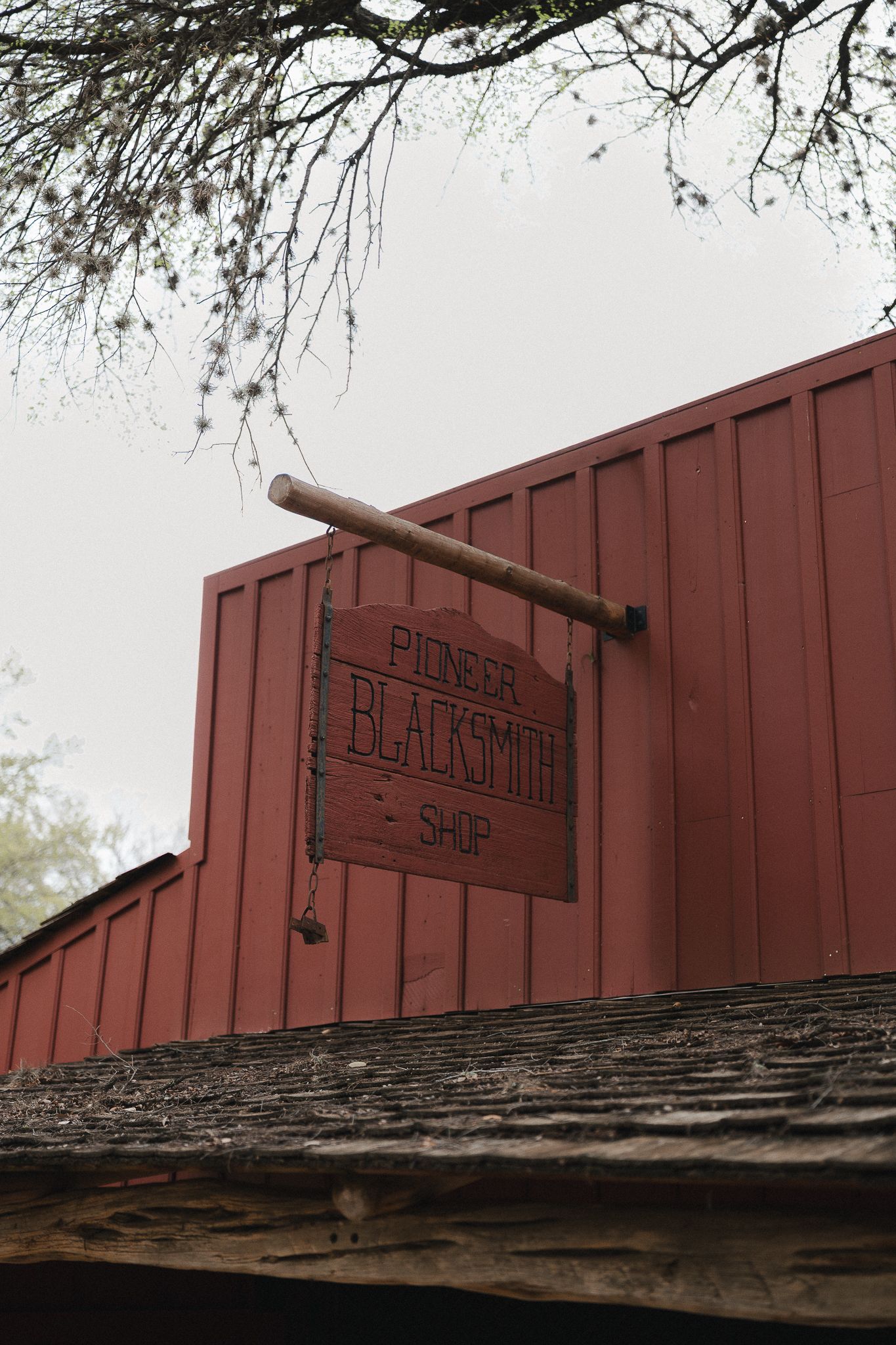 Rustic red wooden Pioneer Blacksmith Shop sign hanging on a historic building exterior on an overcast day.