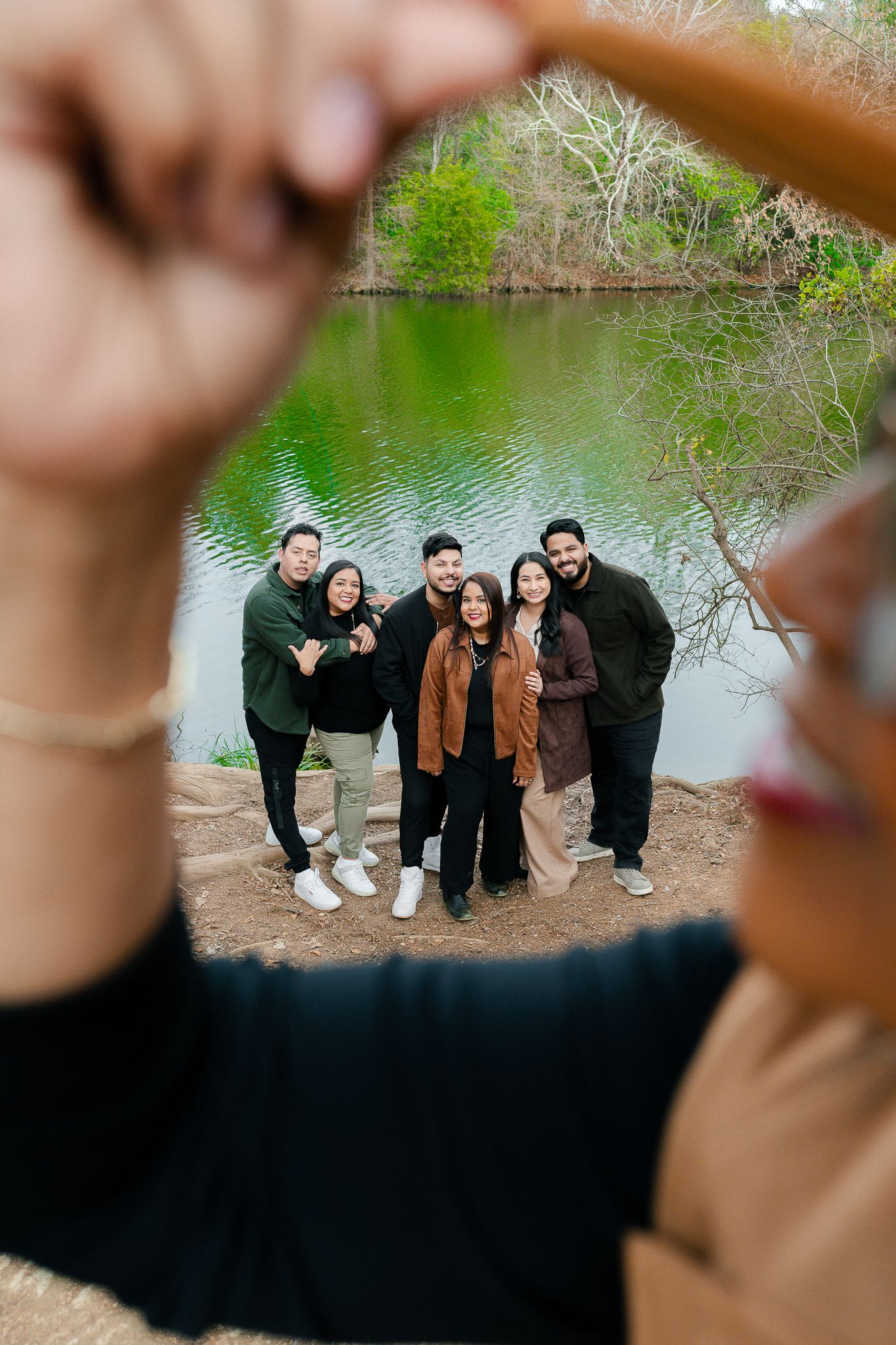 Group photo taken through creative framing of hands making heart shape with pond and trees in background.