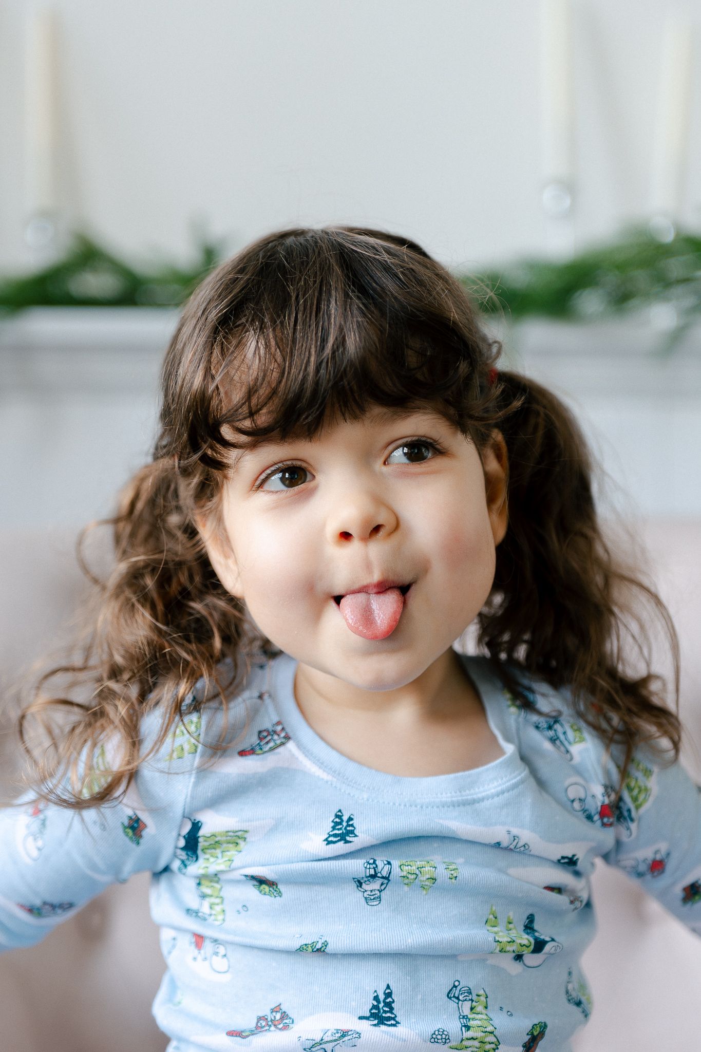 A playful child in a light blue floral shirt sticks out their tongue while making silly faces in a photo series.